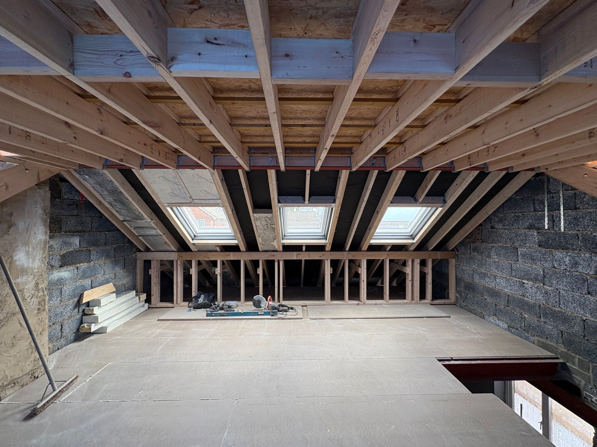 Attic interior under construction: wood framing, skylights, stone walls, and flooring.