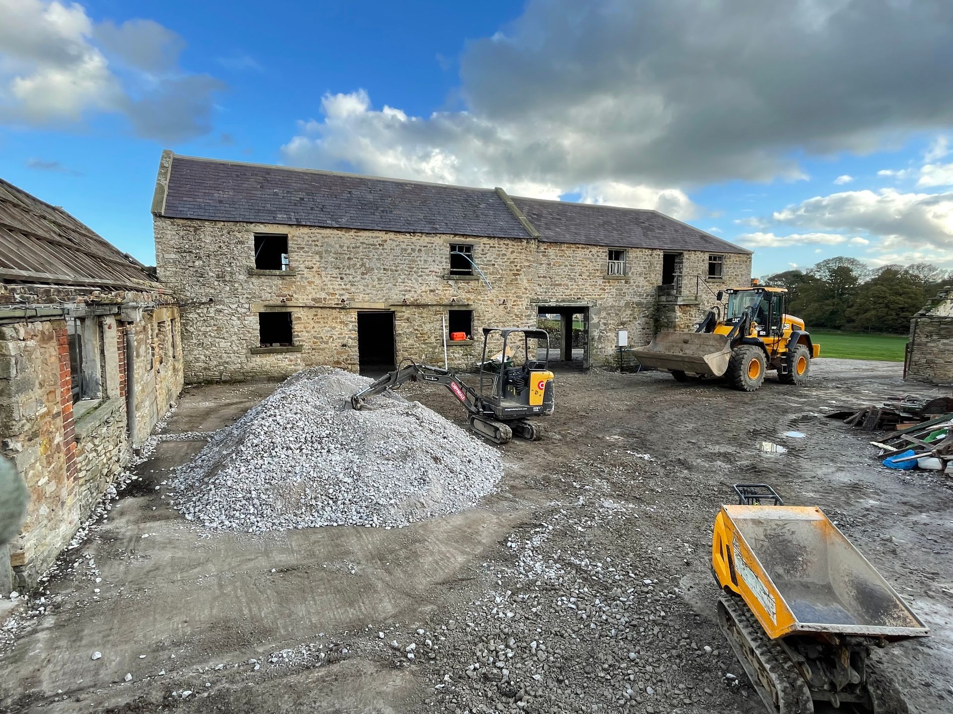 Construction site with stone building, heavy machinery, and pile of debris.