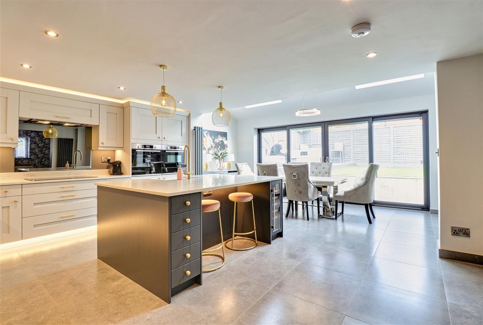 Modern kitchen with island and dining area; gray and white cabinets, gold accents, and large windows.