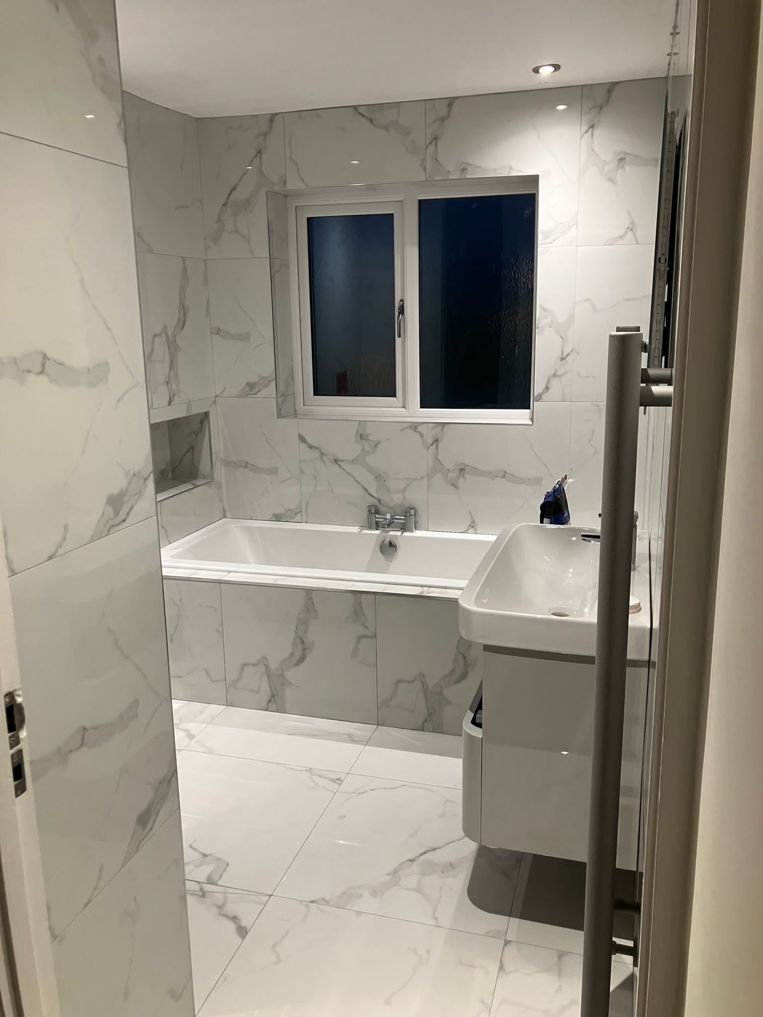 Modern bathroom with marble-patterned tile, a white bathtub, and a floating vanity.