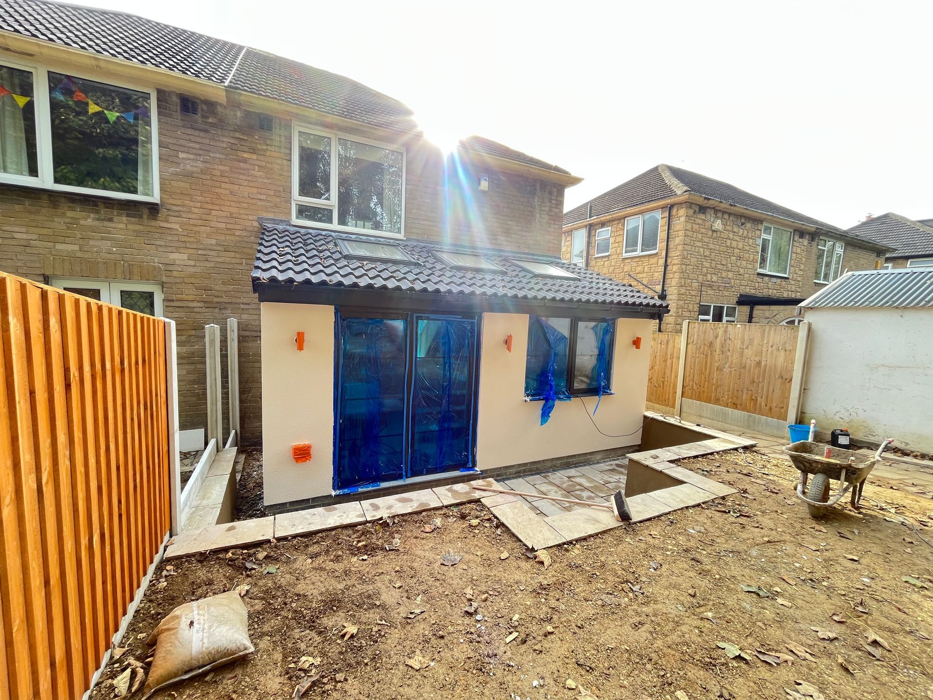 Backyard view of a home extension with beige stucco, blue doors, a skylight, and brown fence.