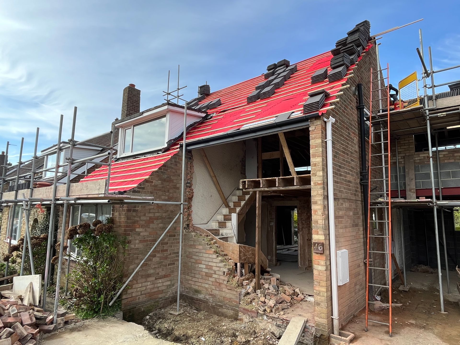House under construction with scaffolding, exposed walls, and new roofing; brick exterior.