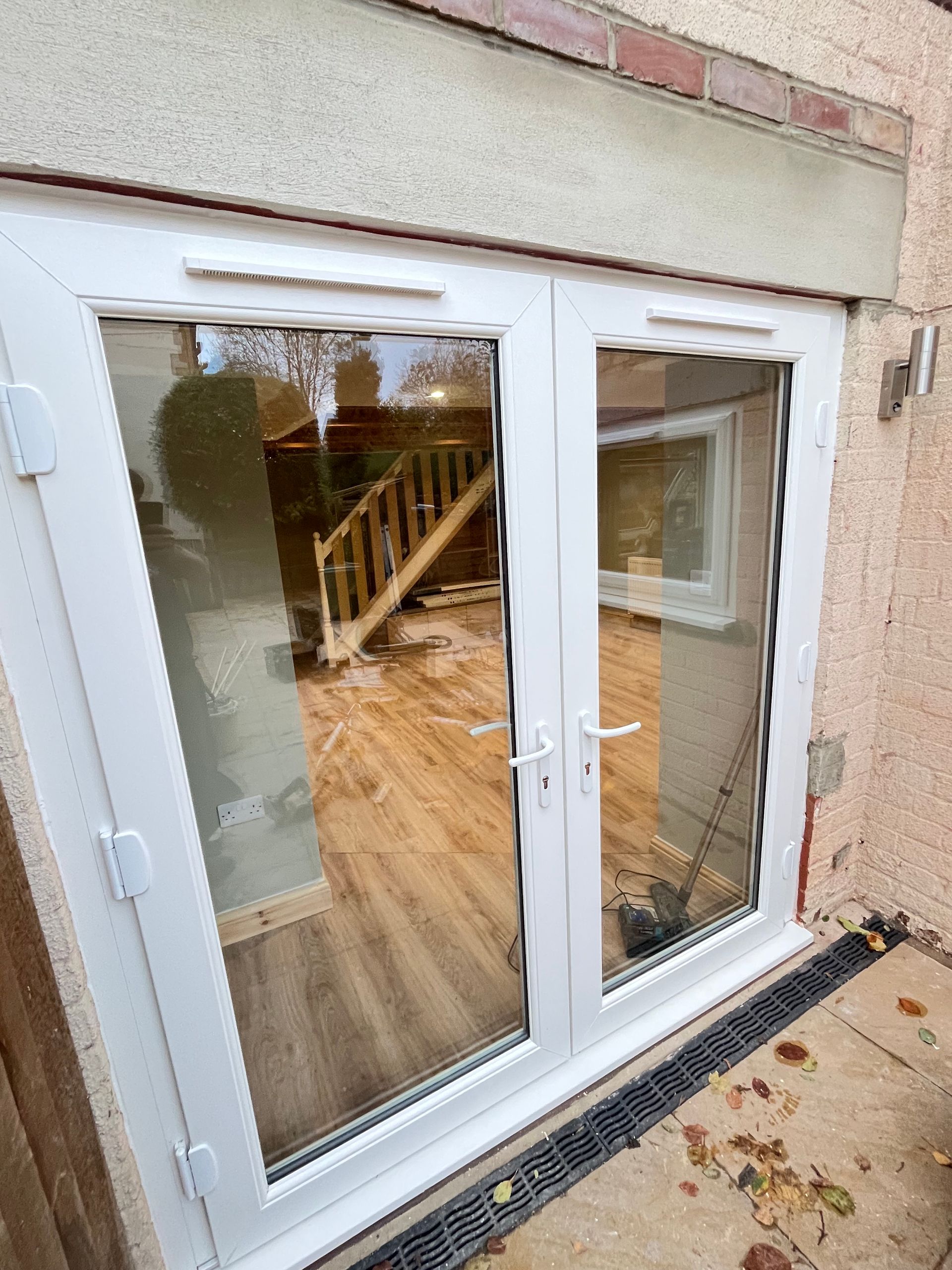 White French doors with large glass panes, reflecting a wooden staircase and interior.