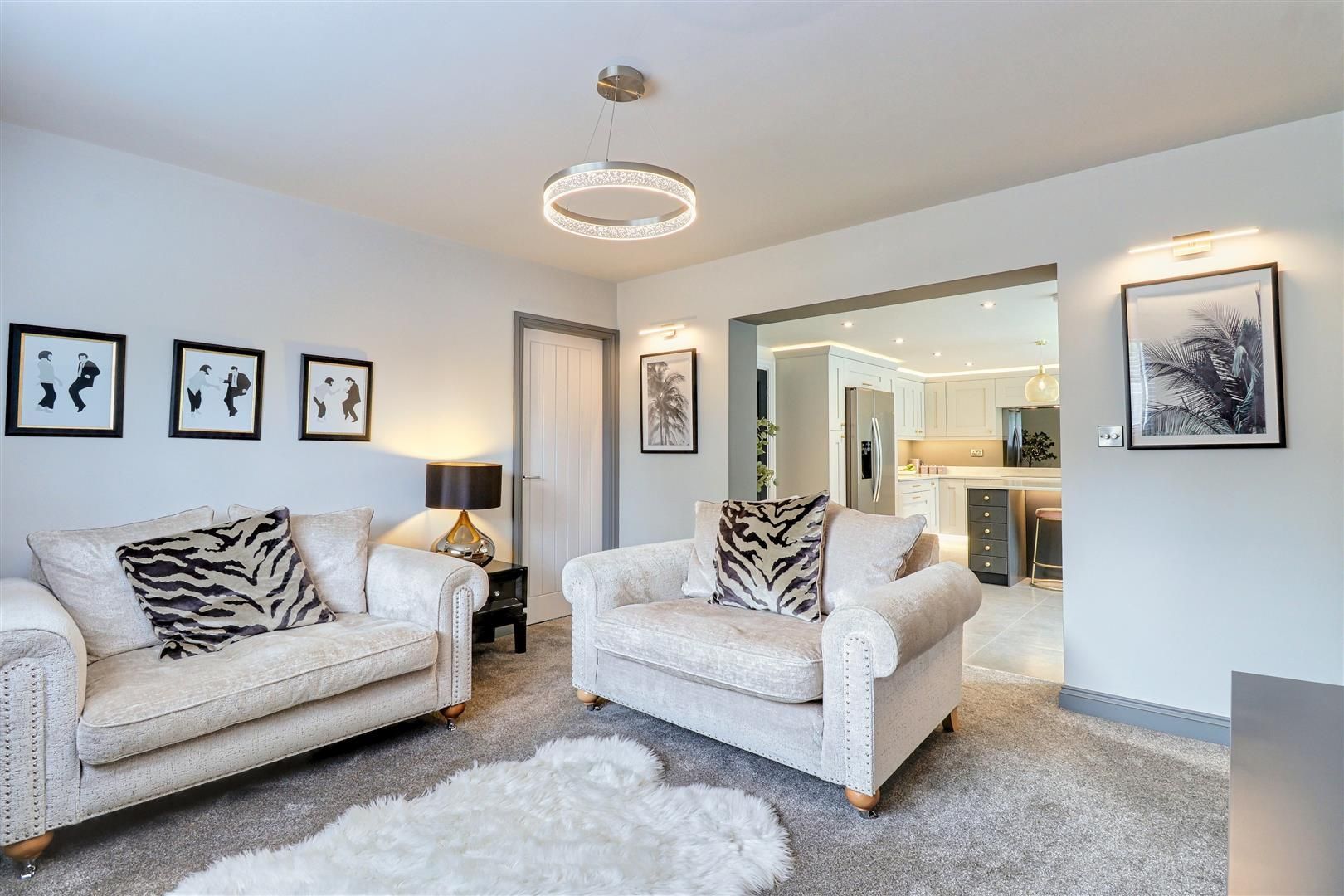 Living room with white sofa, armchair, animal print pillows, and open doorway to kitchen.