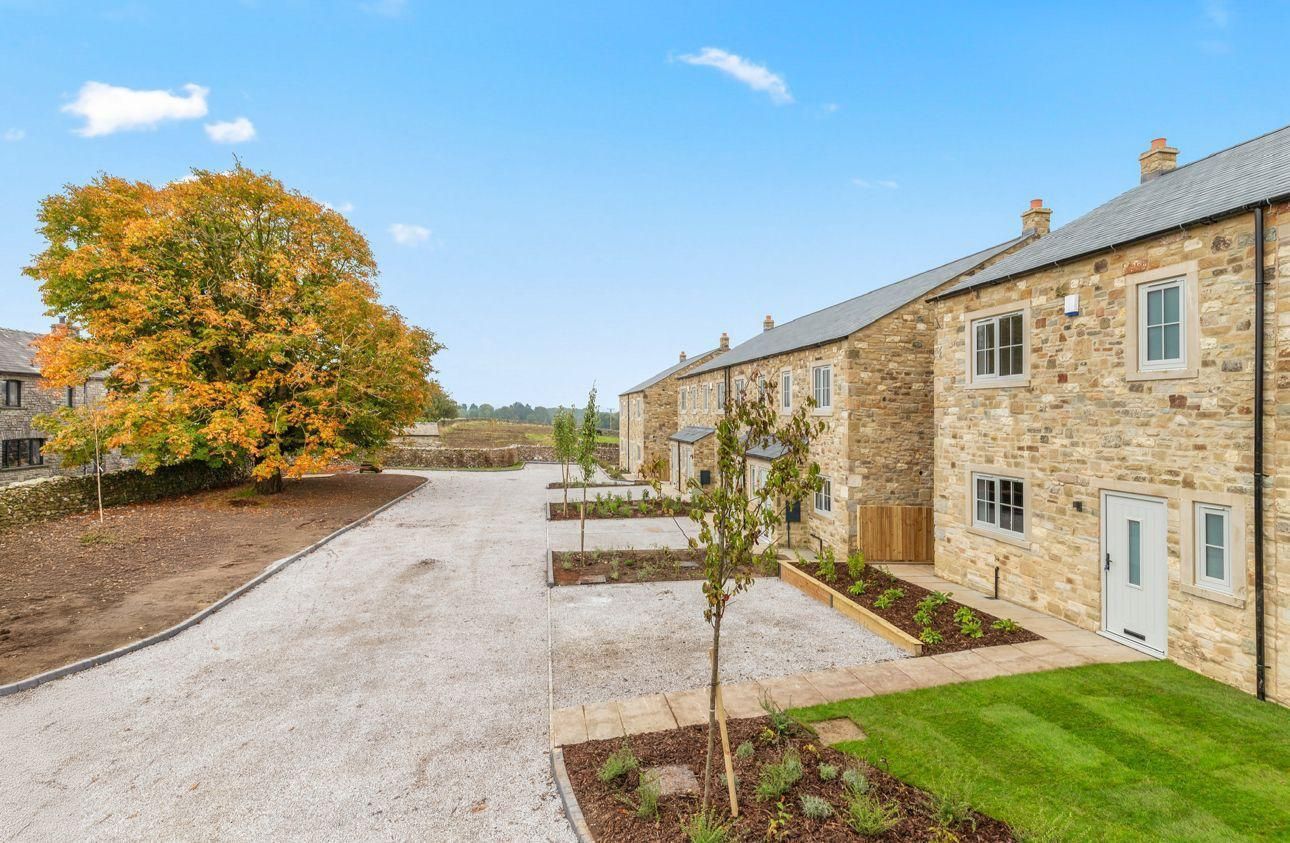 Stone cottages with gravel driveway, green lawn, and fall foliage under a blue sky.