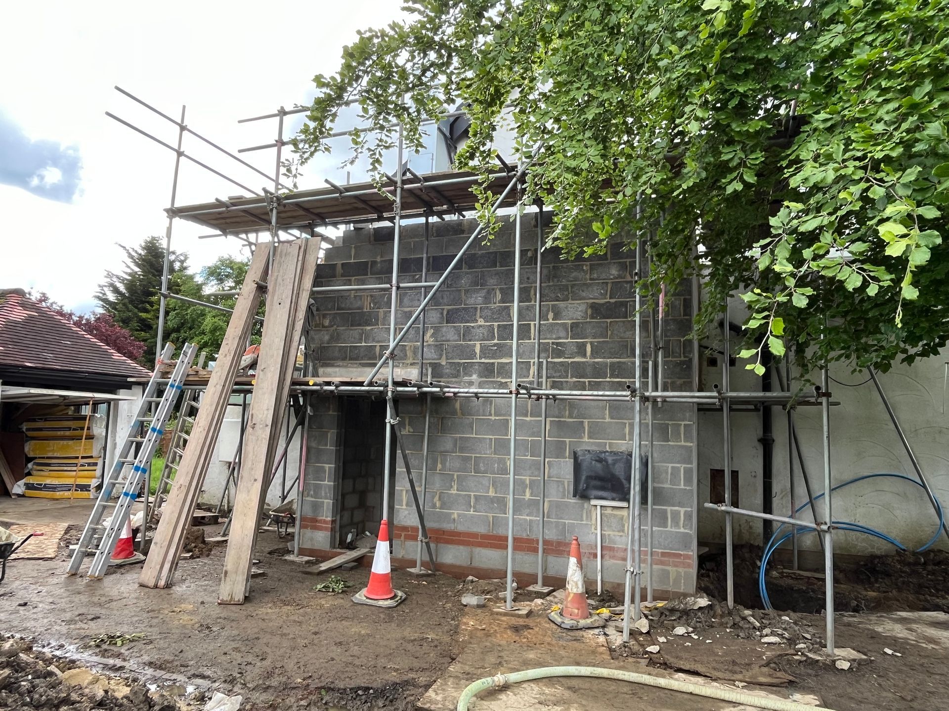 Construction site with scaffolding around a gray block building; a person is working on the roof.