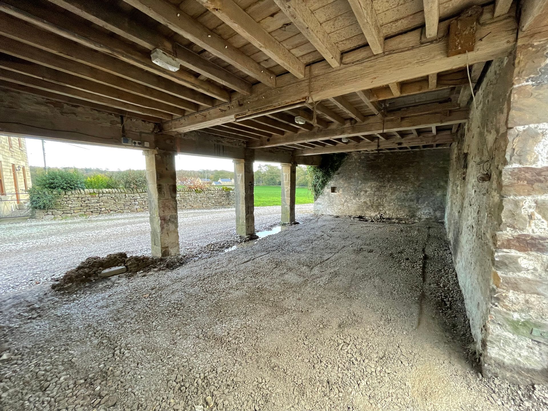 Covered outdoor area with gravel floor, stone walls, and wooden beams overhead.