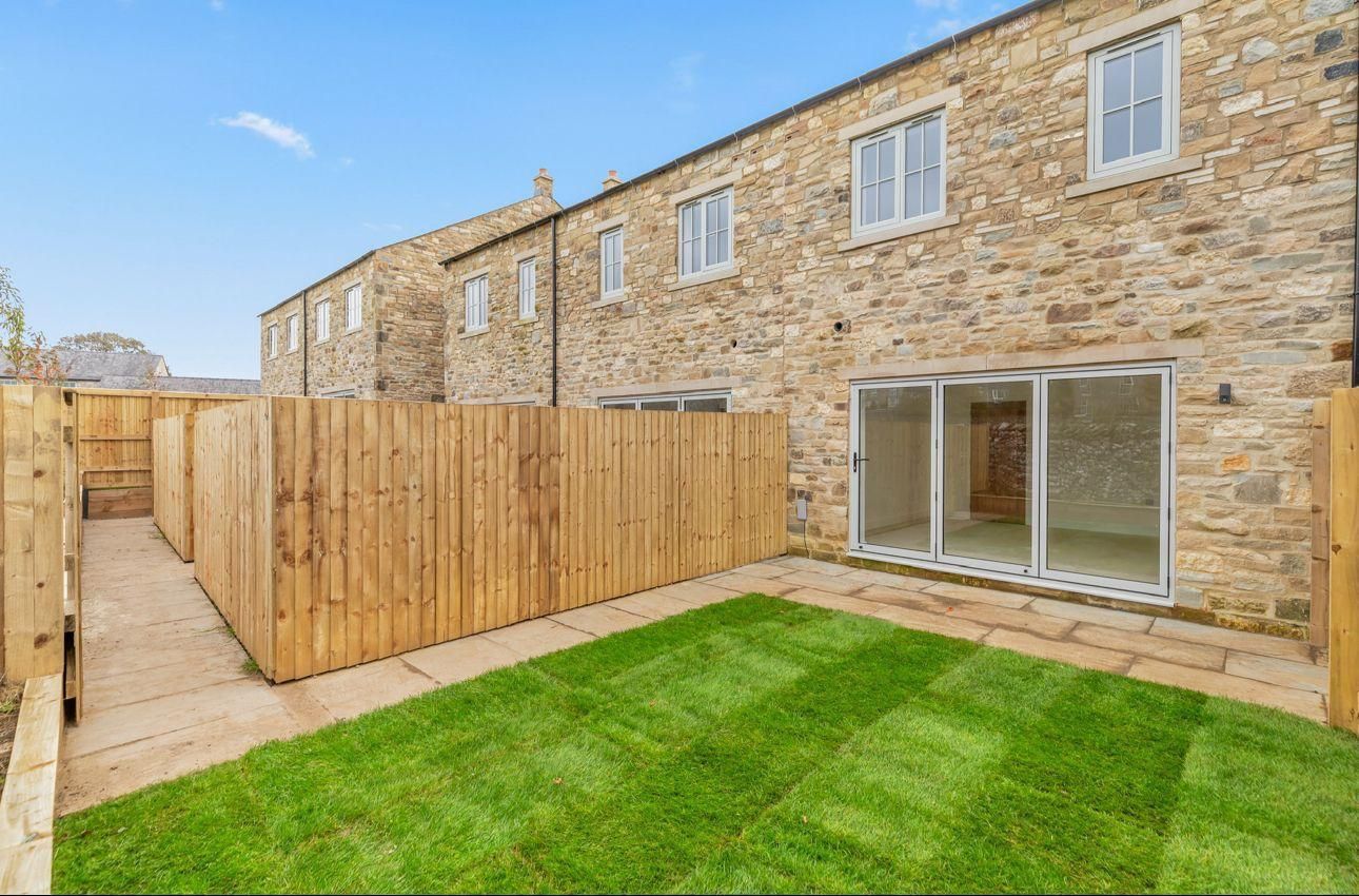 Backyard of a stone house with a lawn, wooden fence, and glass doors.