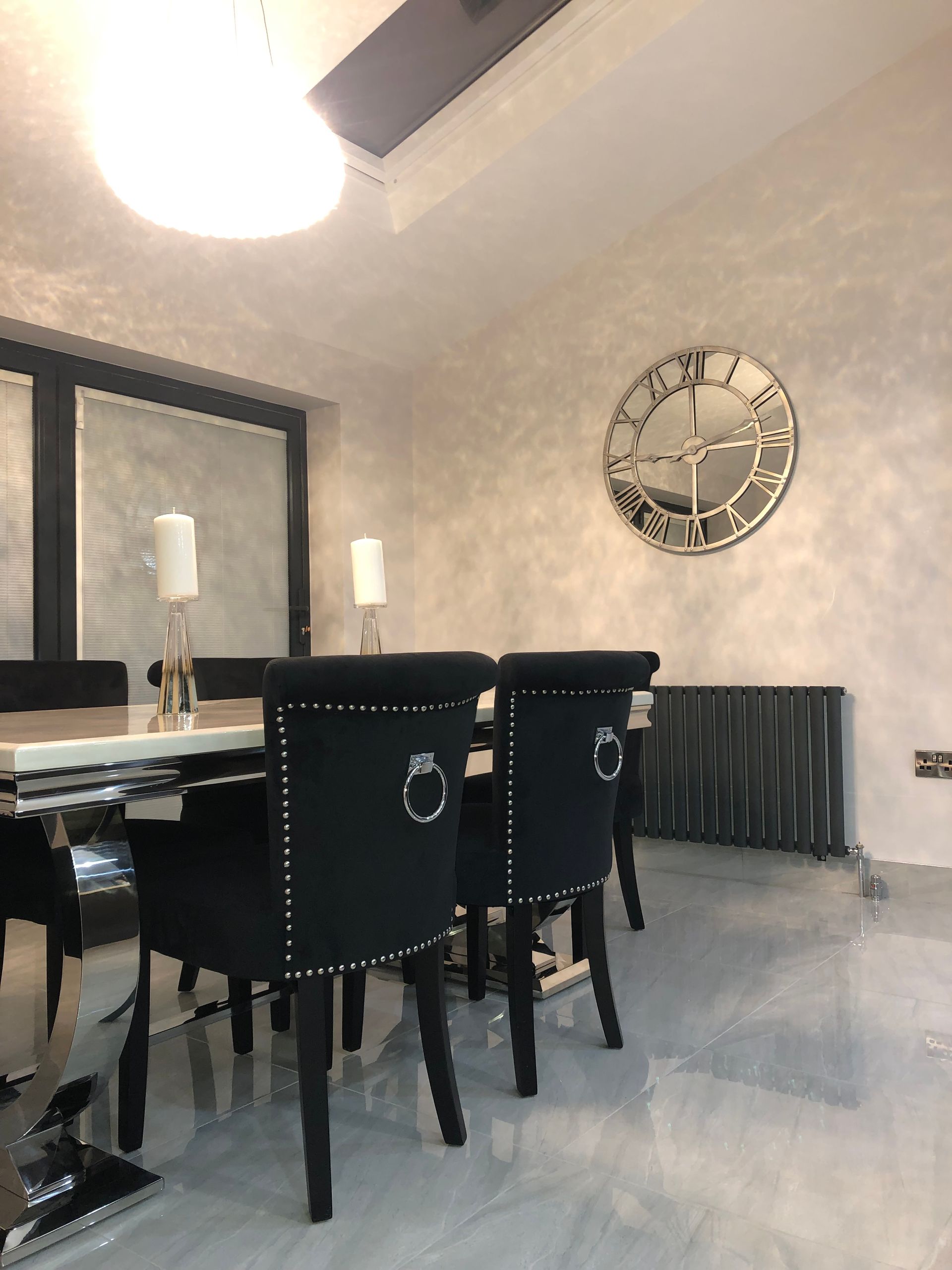 Dining room with black chairs, a marble table, and a large silver clock.