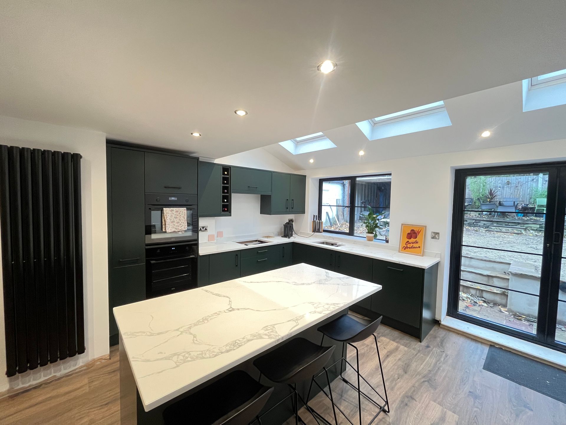 Modern kitchen with dark green cabinets, white countertops, island with seating, and skylights.
