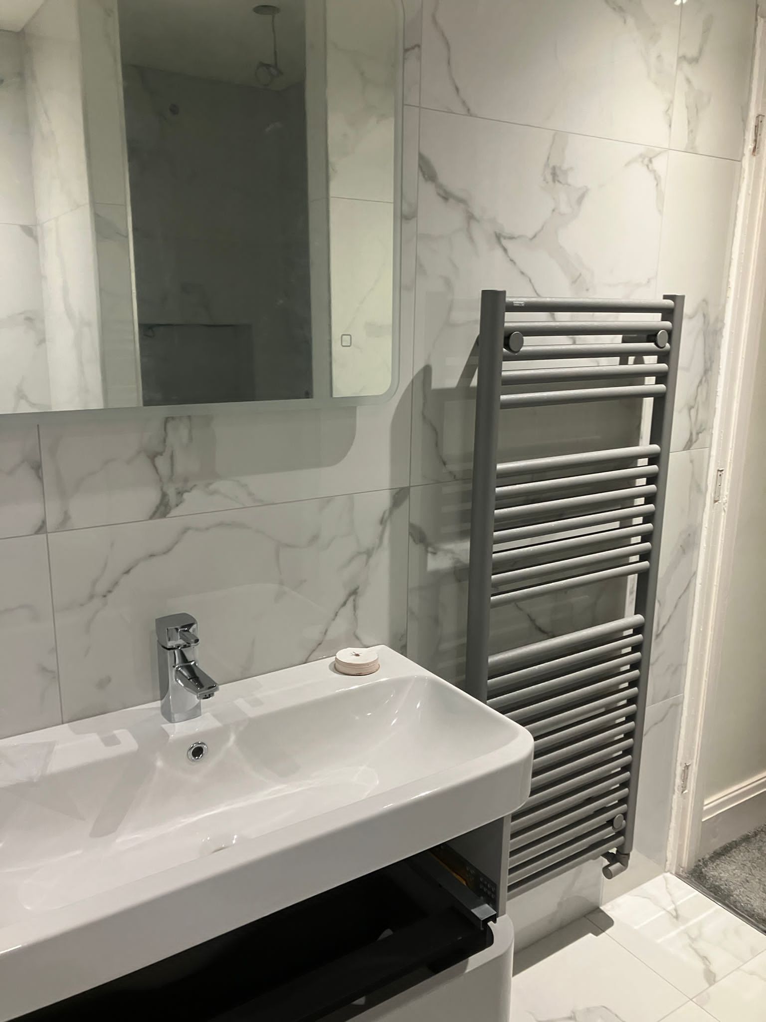 Bathroom with white marble tile walls, a sink, mirror, and a gray towel warmer.