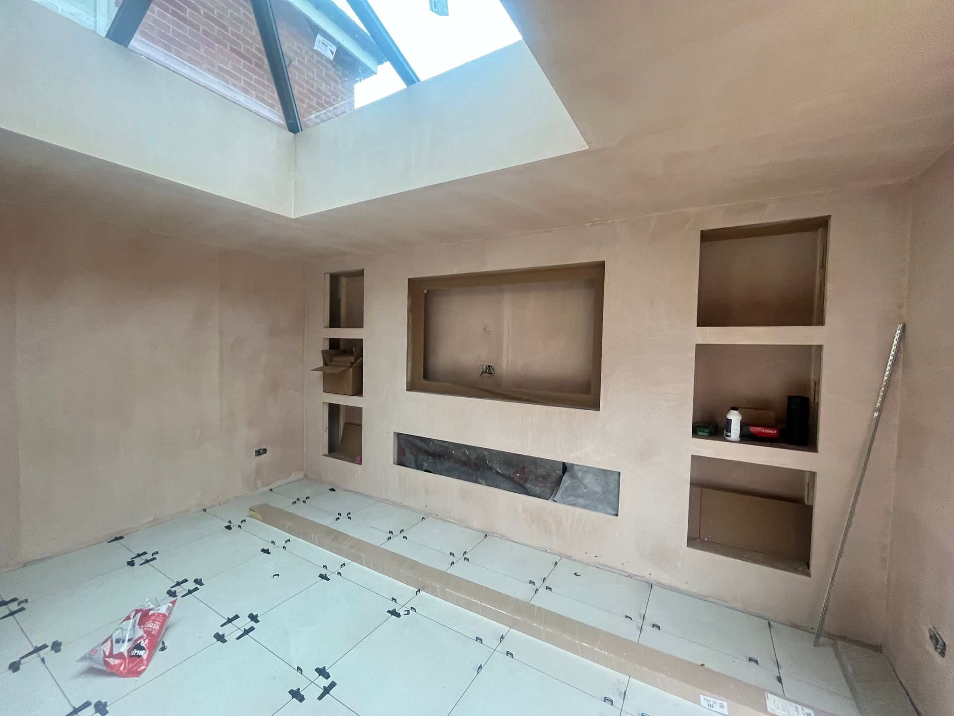 Interior room with finished plaster walls, alcoves, and tiled floor. Natural light from skylight.