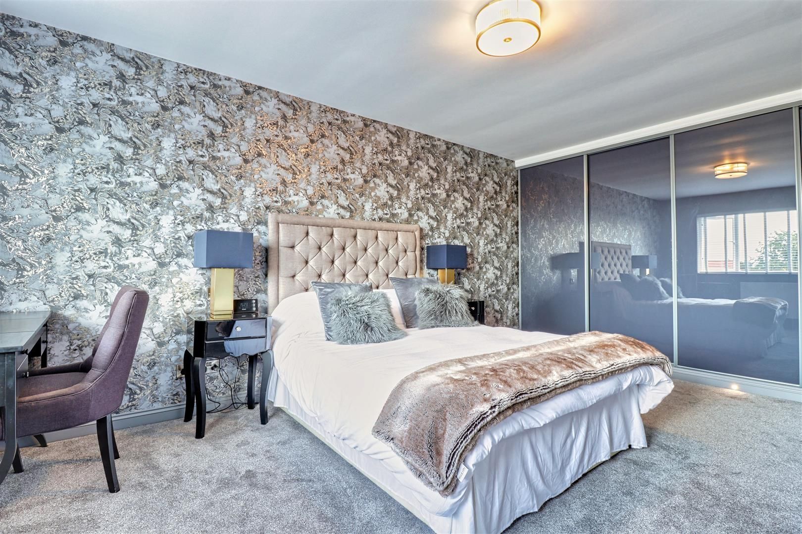 Bedroom with textured gray wallpaper, tufted headboard, dark furniture, and sliding door closet.