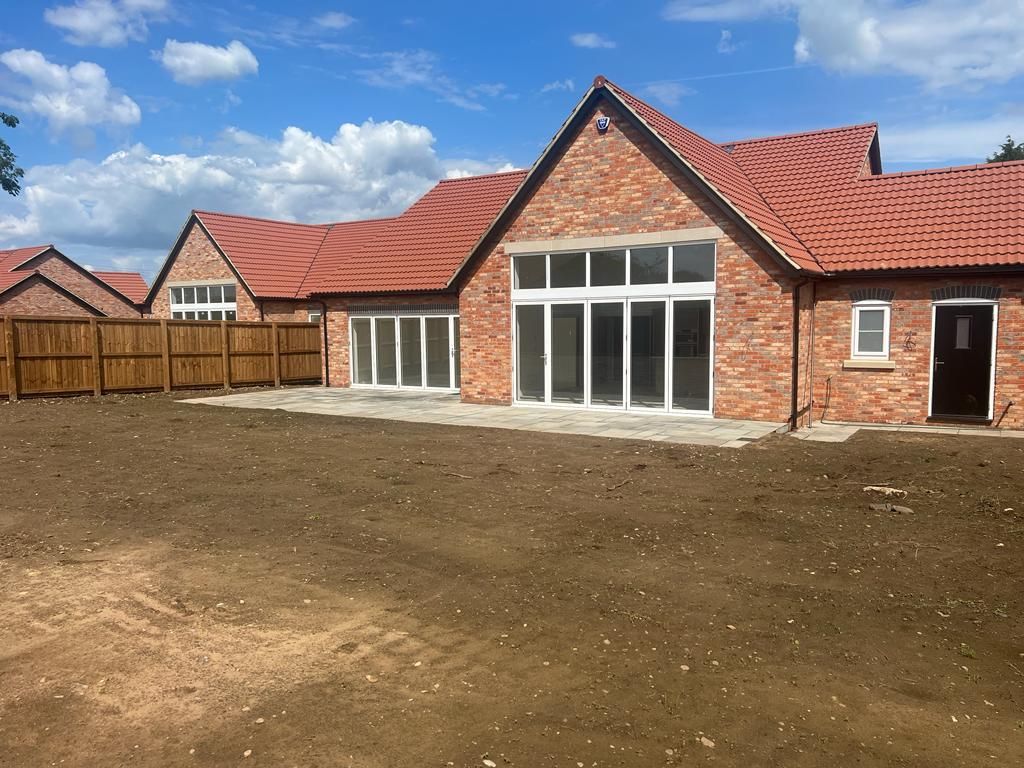 Brick building with red roof, large windows, and a brown fence in front. Brown dirt area.