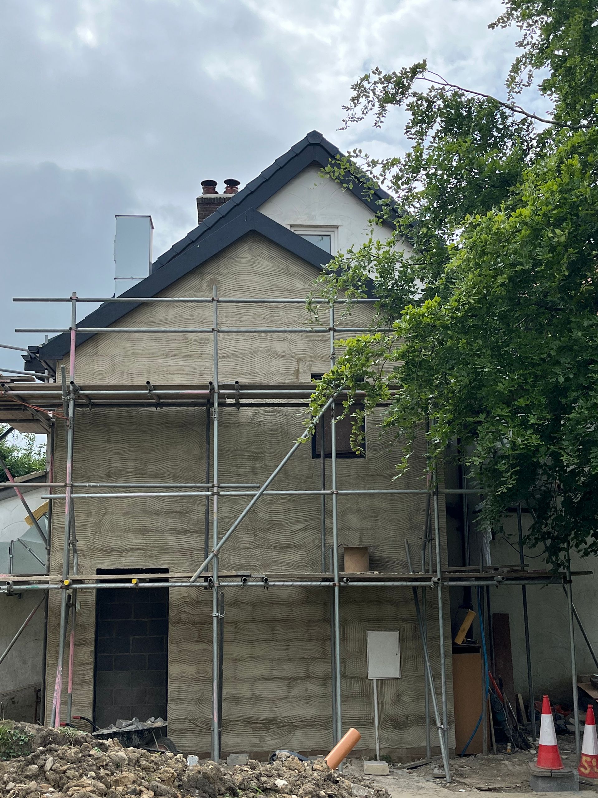 House exterior under construction, covered in scaffolding, cloudy sky, trees.