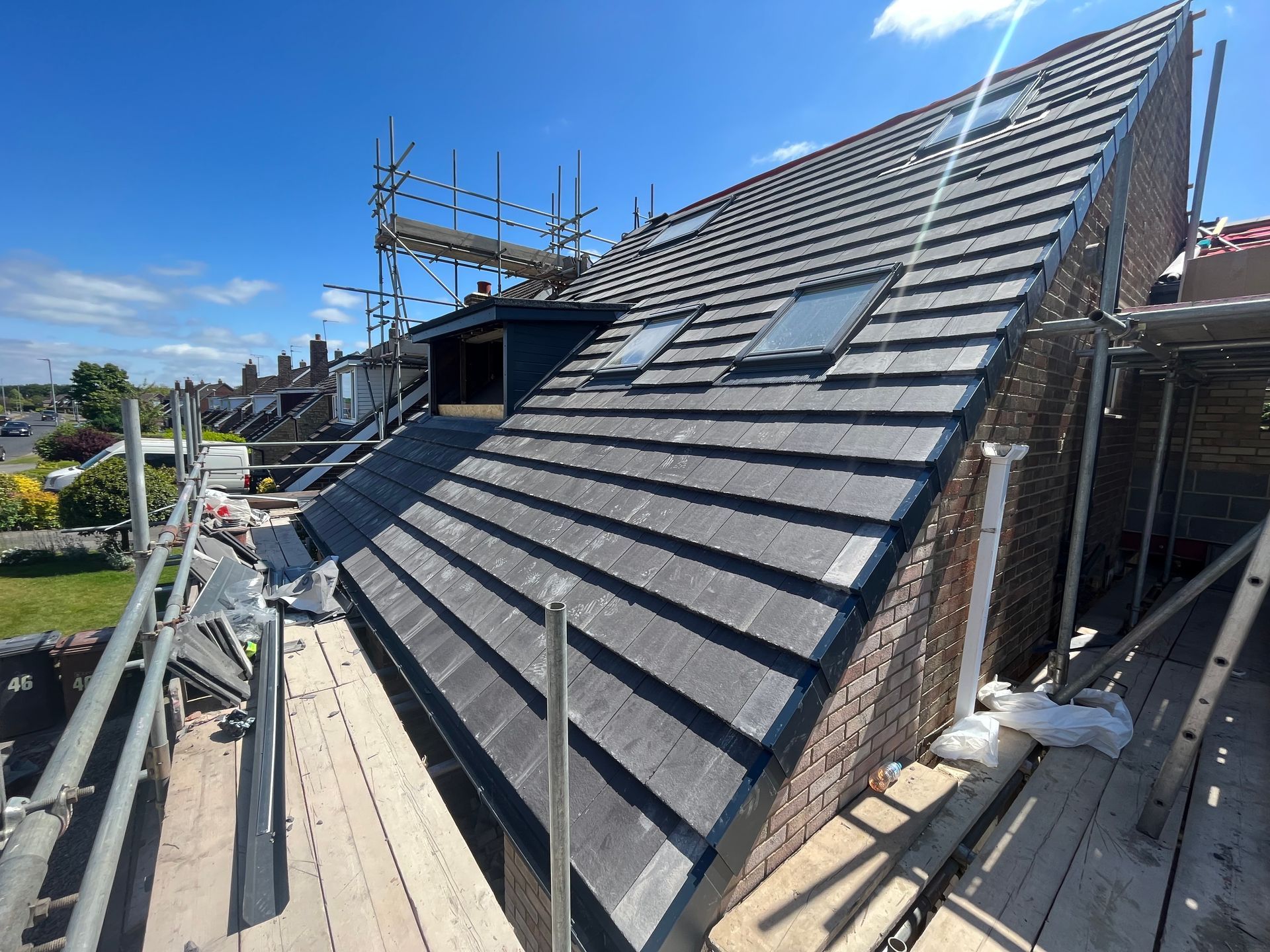 A roof under construction with scaffolding, gray tiles, dormer windows, and a blue sky.