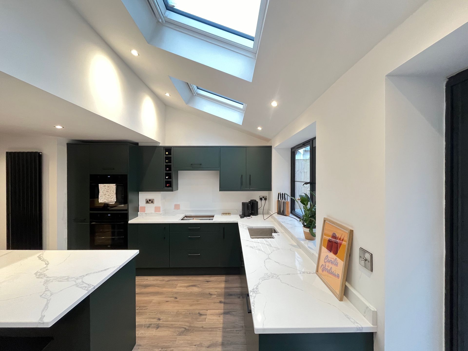Modern kitchen with dark green cabinets, white countertops, and skylights.