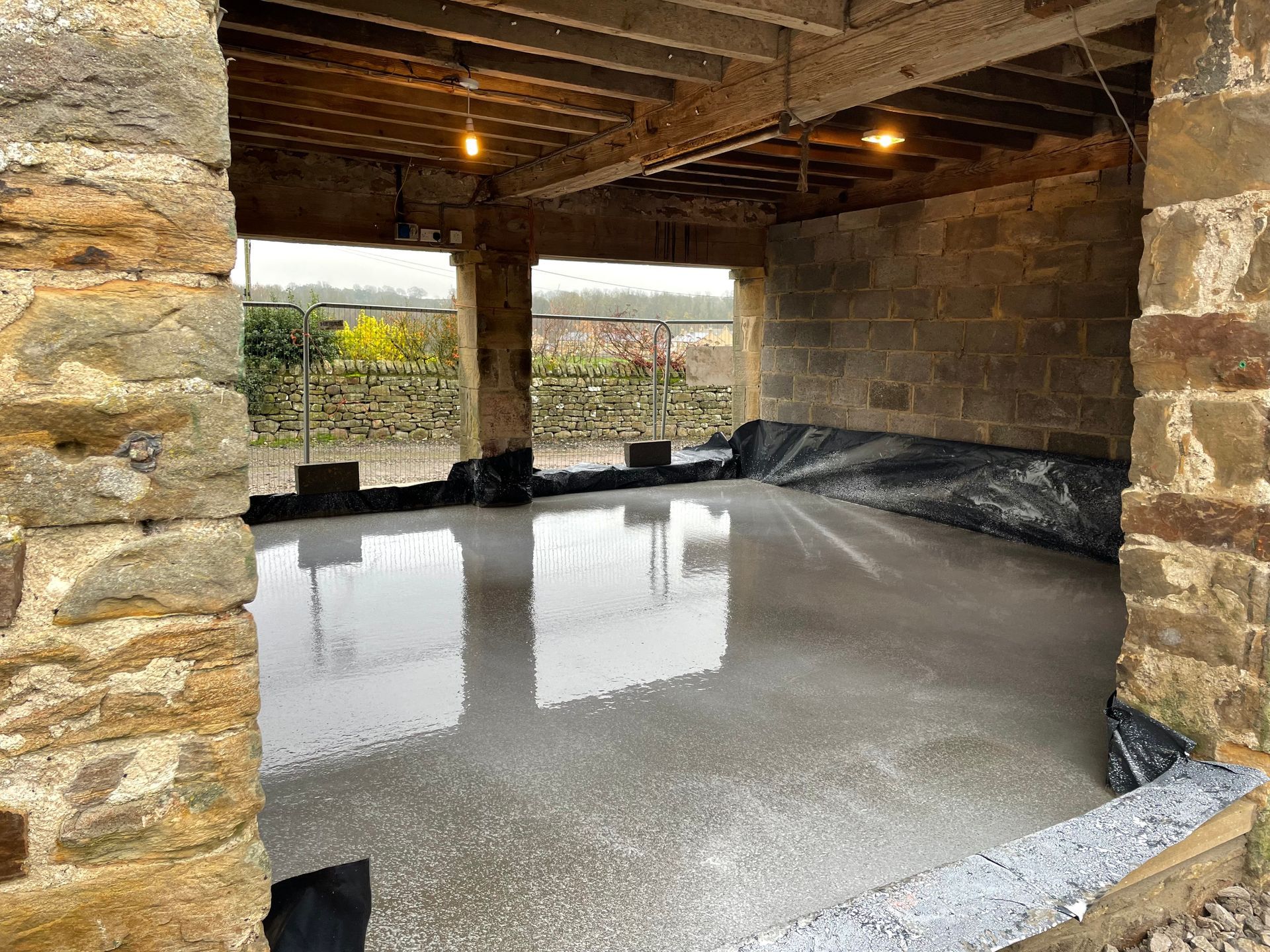 Concrete floor poured inside a stone building, under a wooden beam ceiling.