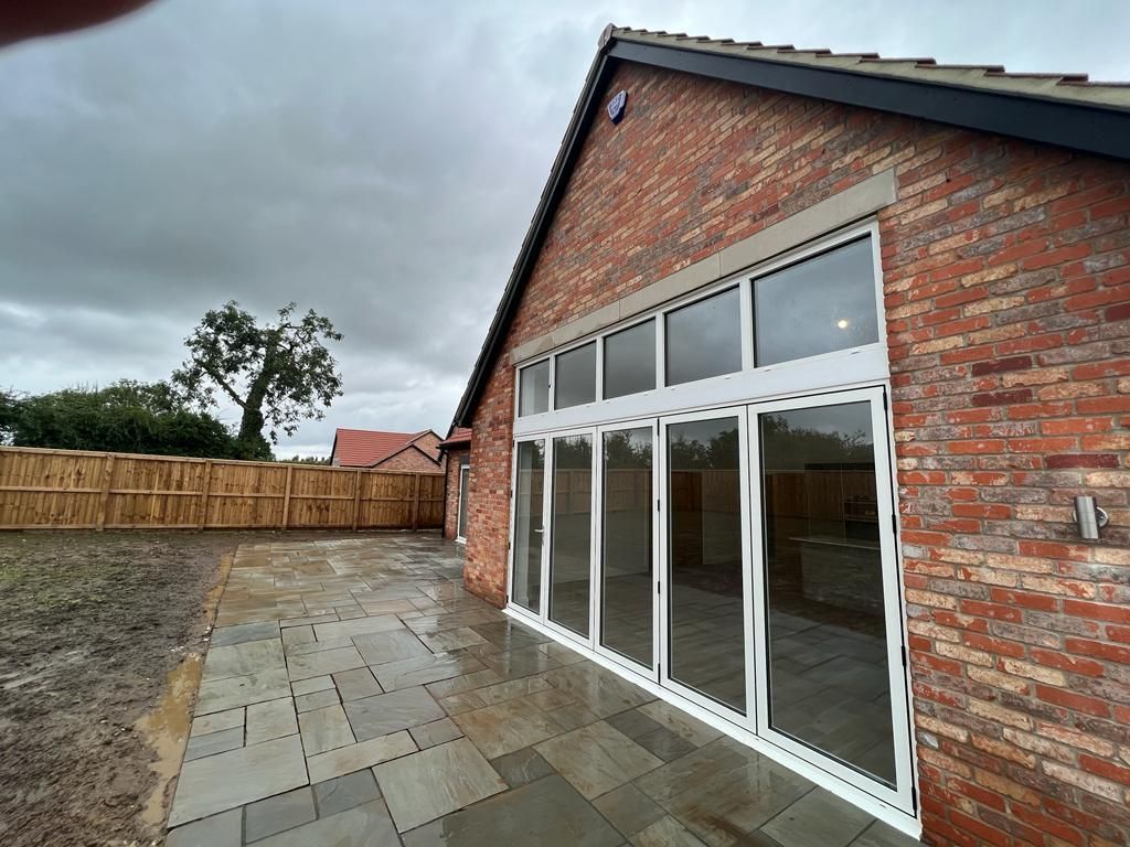 Exterior of a brick house with large glass doors opening onto a patio. Cloudy sky.