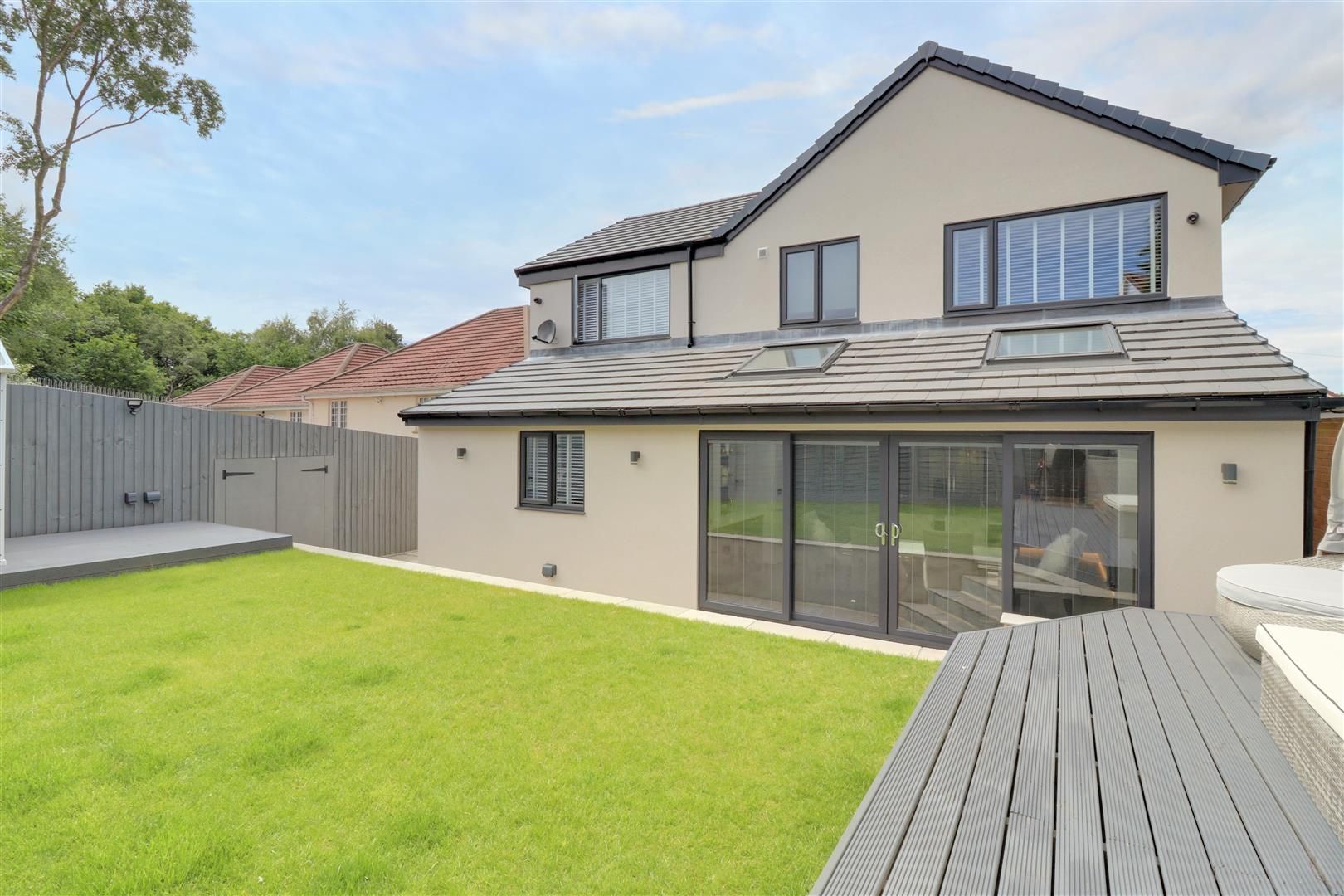 Two-story house with sliding glass doors, gray roof, and green lawn. Gray wooden deck in foreground.