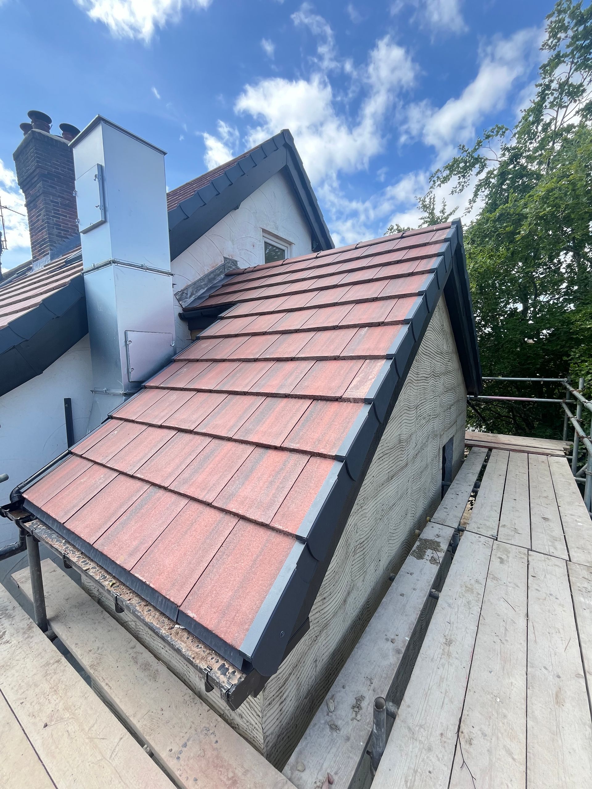 Red-tiled roof on a house, black trim, scaffolding, blue sky.
