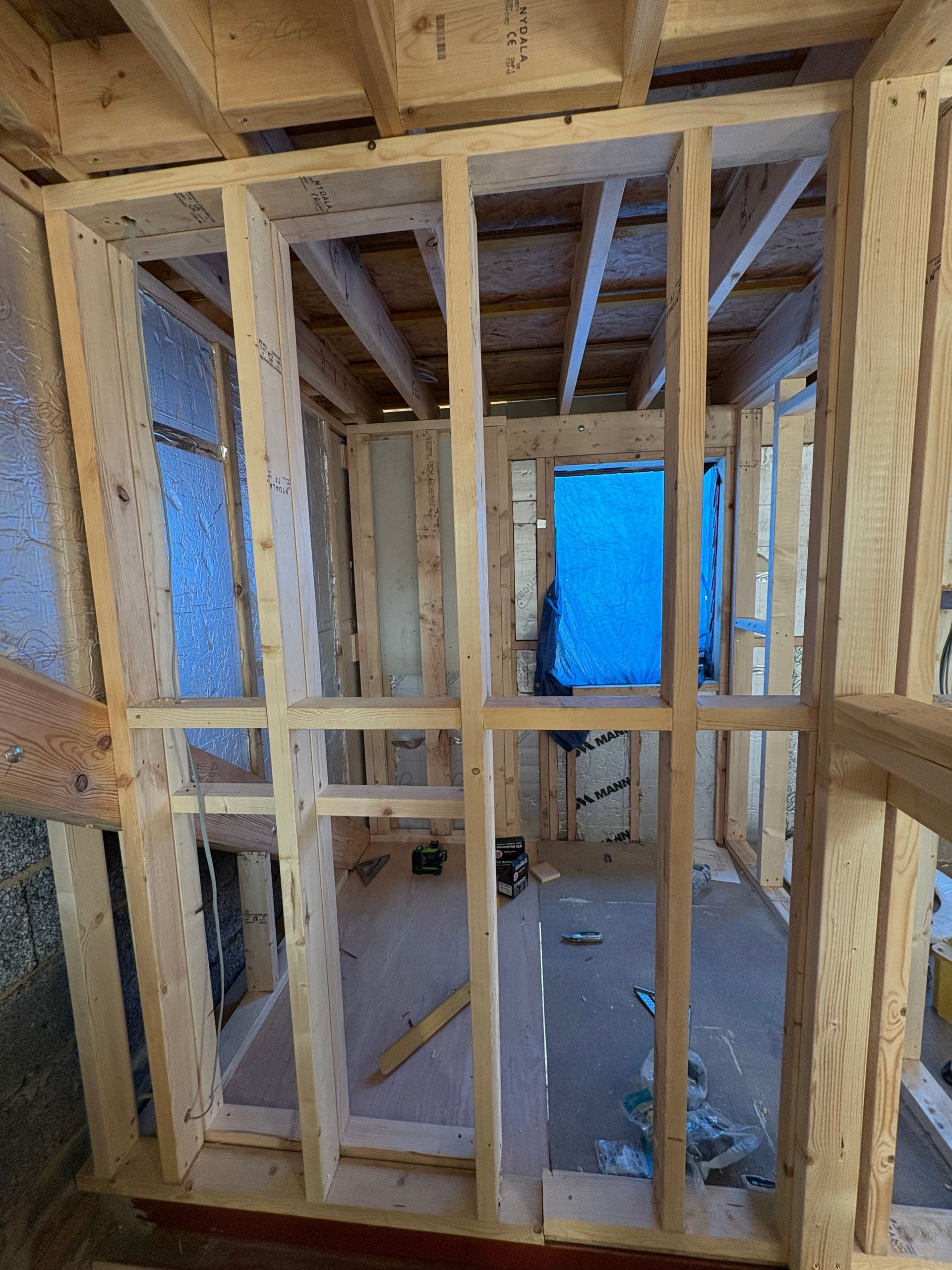 Wooden framing of a small room under construction, with a doorway and window openings.