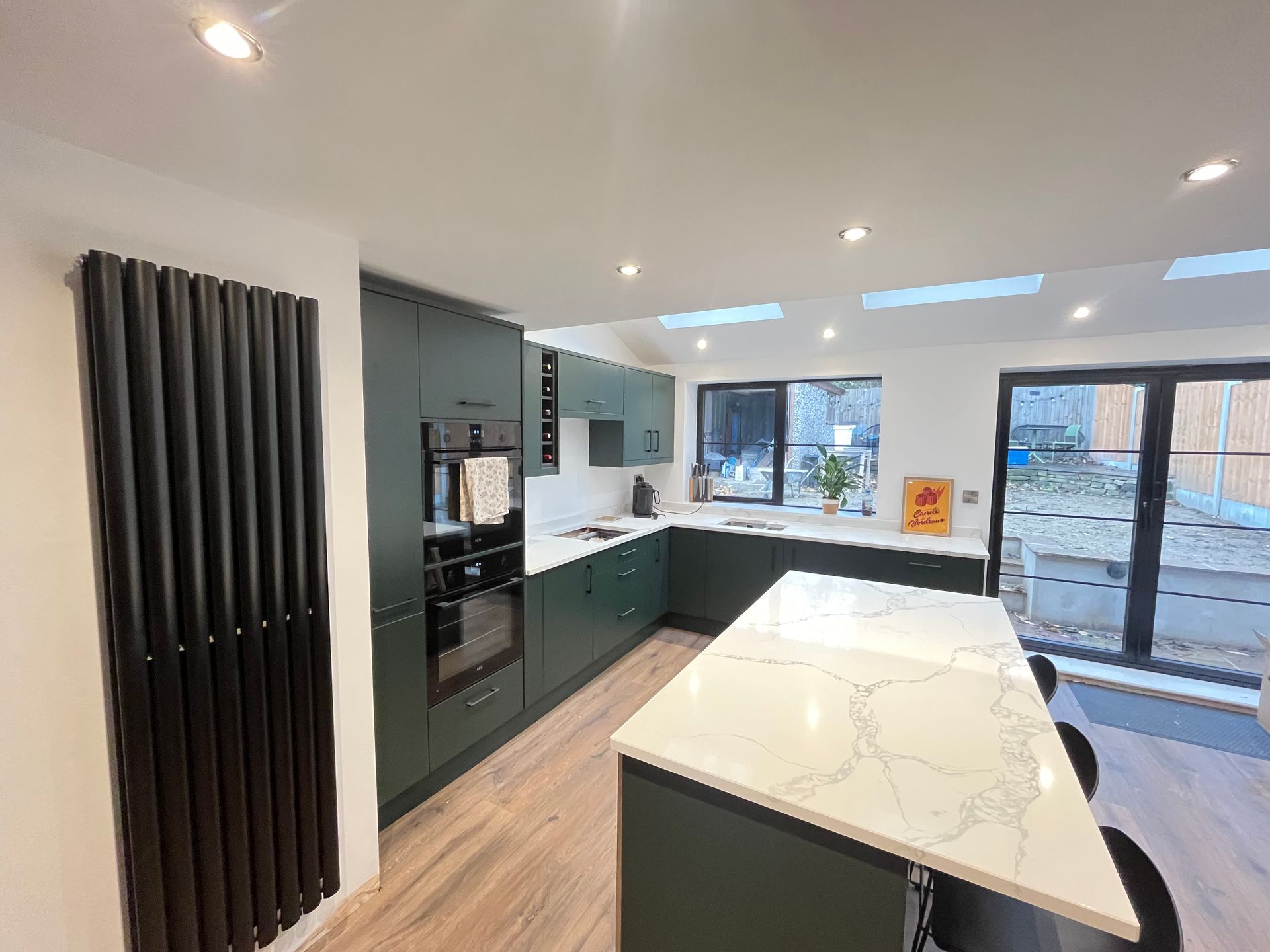 Green modern kitchen with island, white countertops, and black radiator.