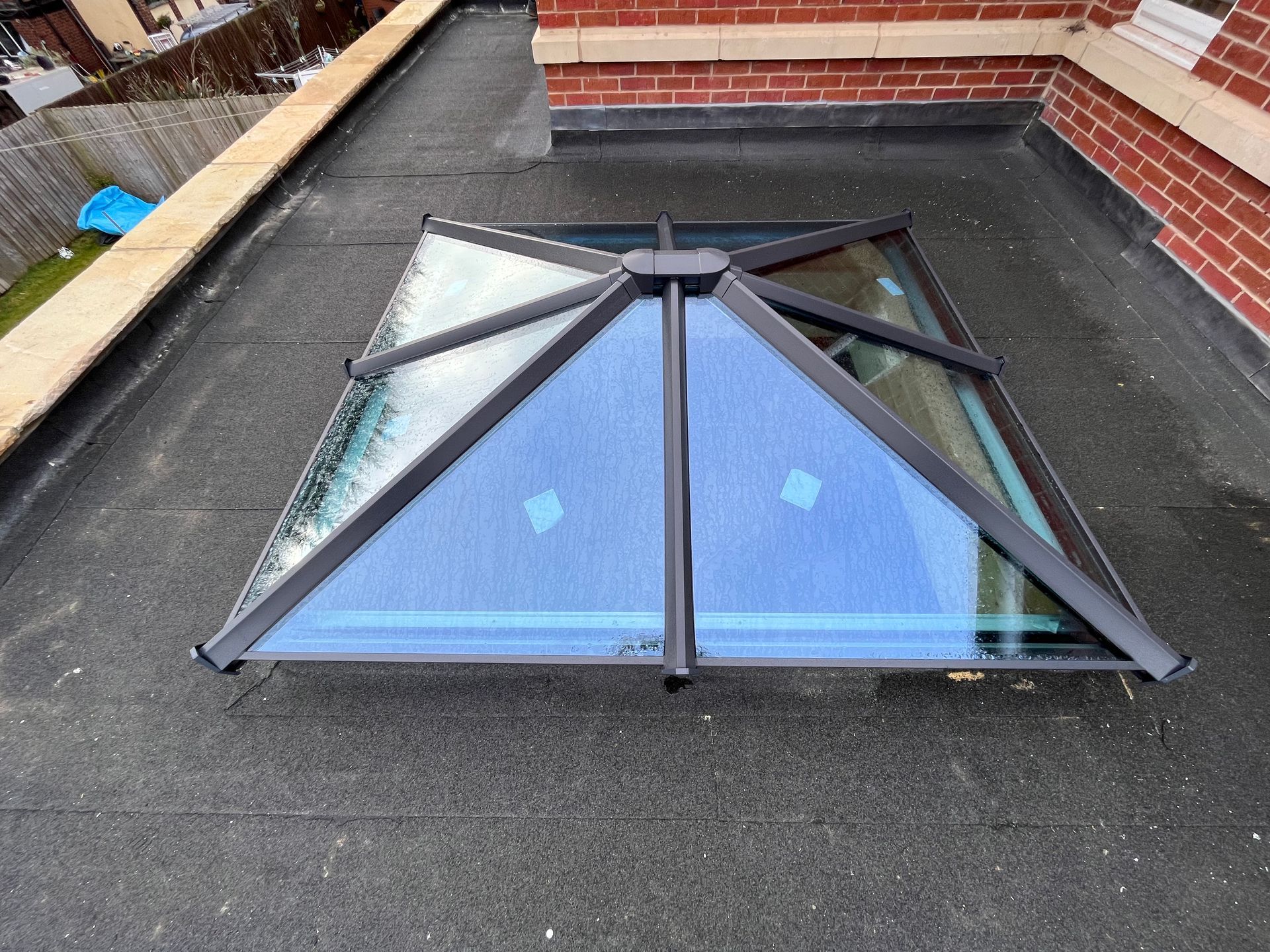 A rectangular skylight with a black frame on a flat black roof next to a brick wall.