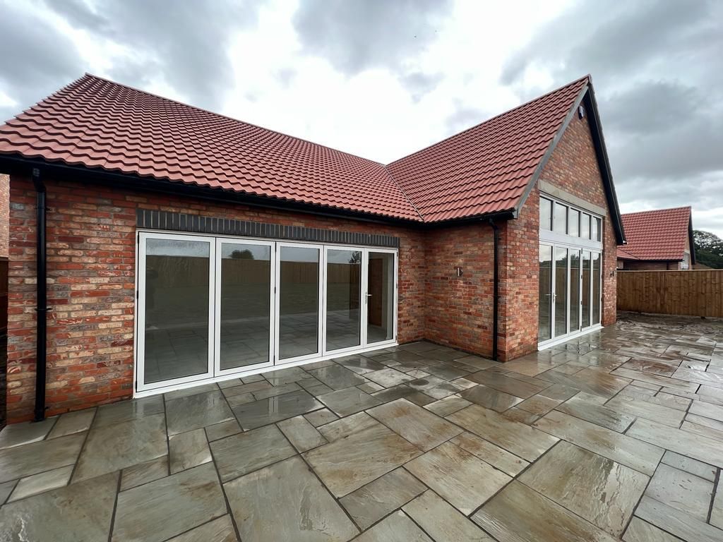 Brick building with red tile roof, large glass doors, and stone patio. Cloudy sky.