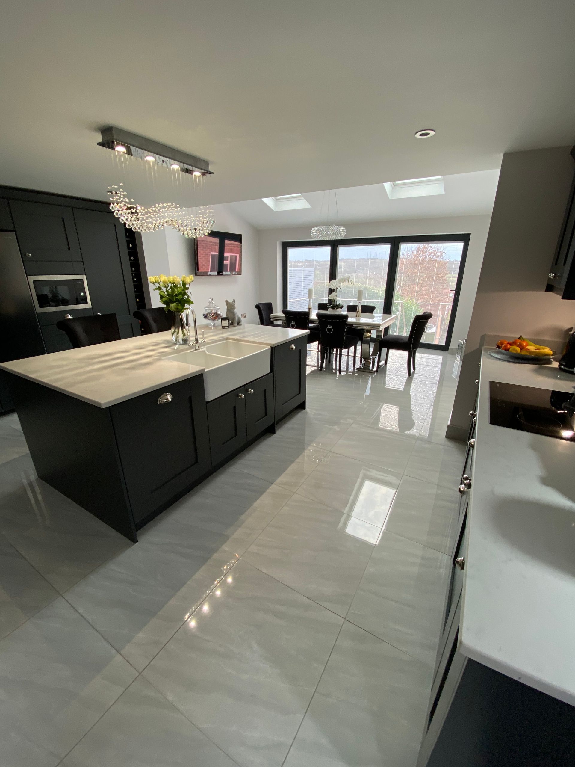 Modern kitchen with dark cabinets, white island, and dining area with large windows.