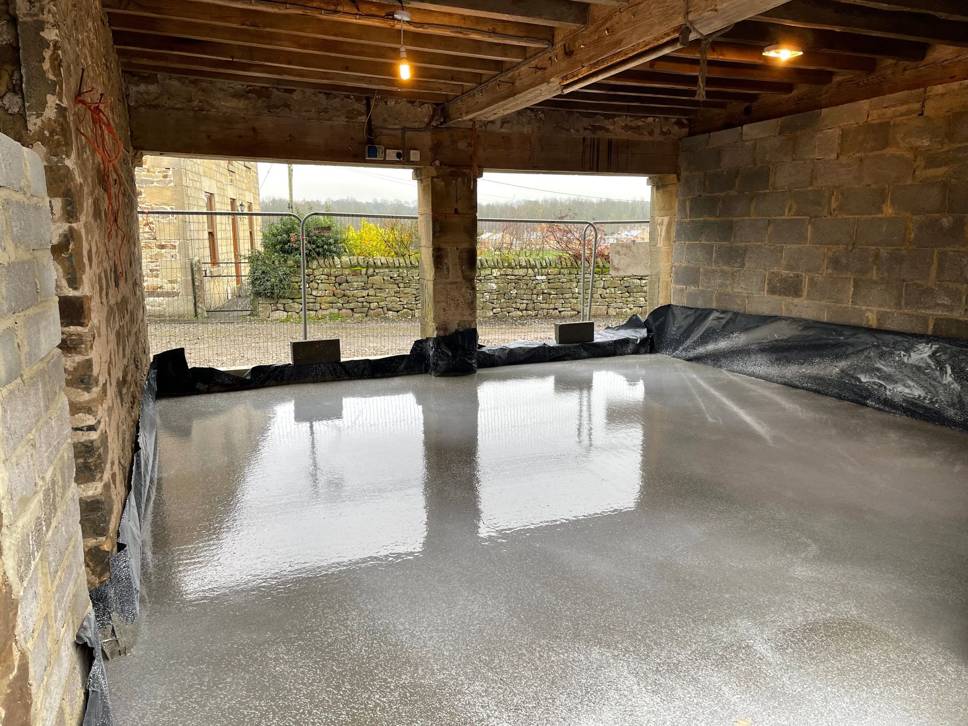 Newly poured concrete floor in a building with exposed brick and a view of the outside.