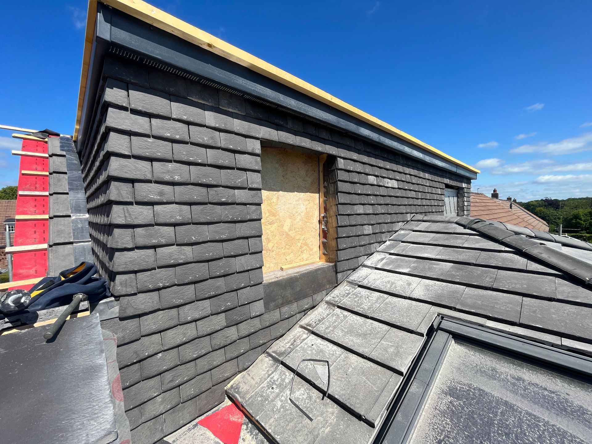Rooftop construction: Dark gray shingle siding installed on dormer, with a clear blue sky above.