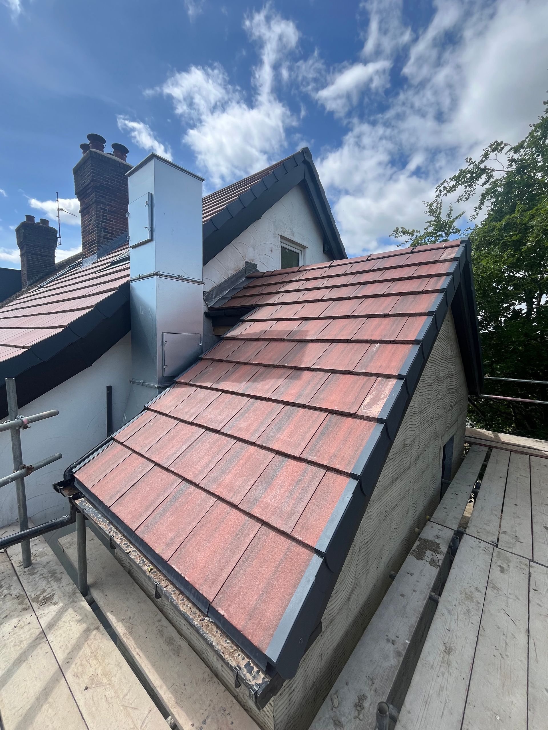 Roof of a house with red tiles and black trim, scaffolding, chimney, and blue sky.