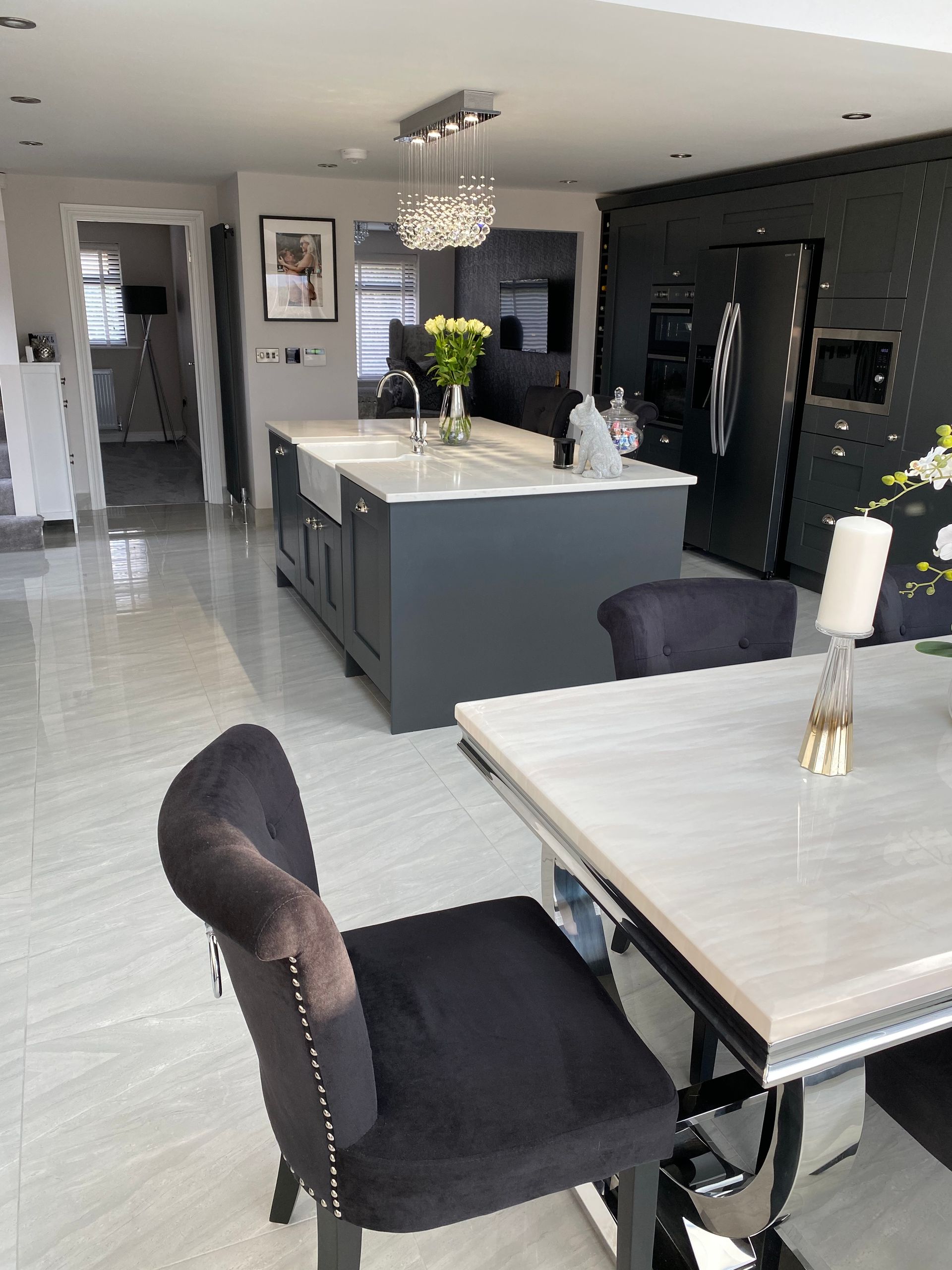 Modern kitchen: grey cabinets, island, marble table with black chairs, silver appliances, and white floors.