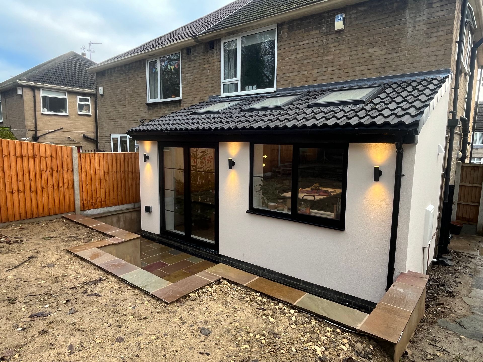 Rear extension on a house with black-framed windows, roof lights, and cream stucco exterior.