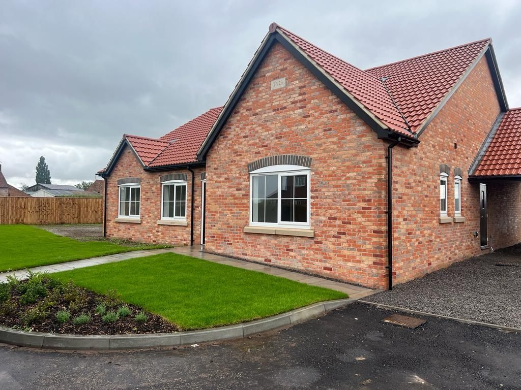 Brick bungalow with red tiled roof, white windows, and green lawn on an overcast day.