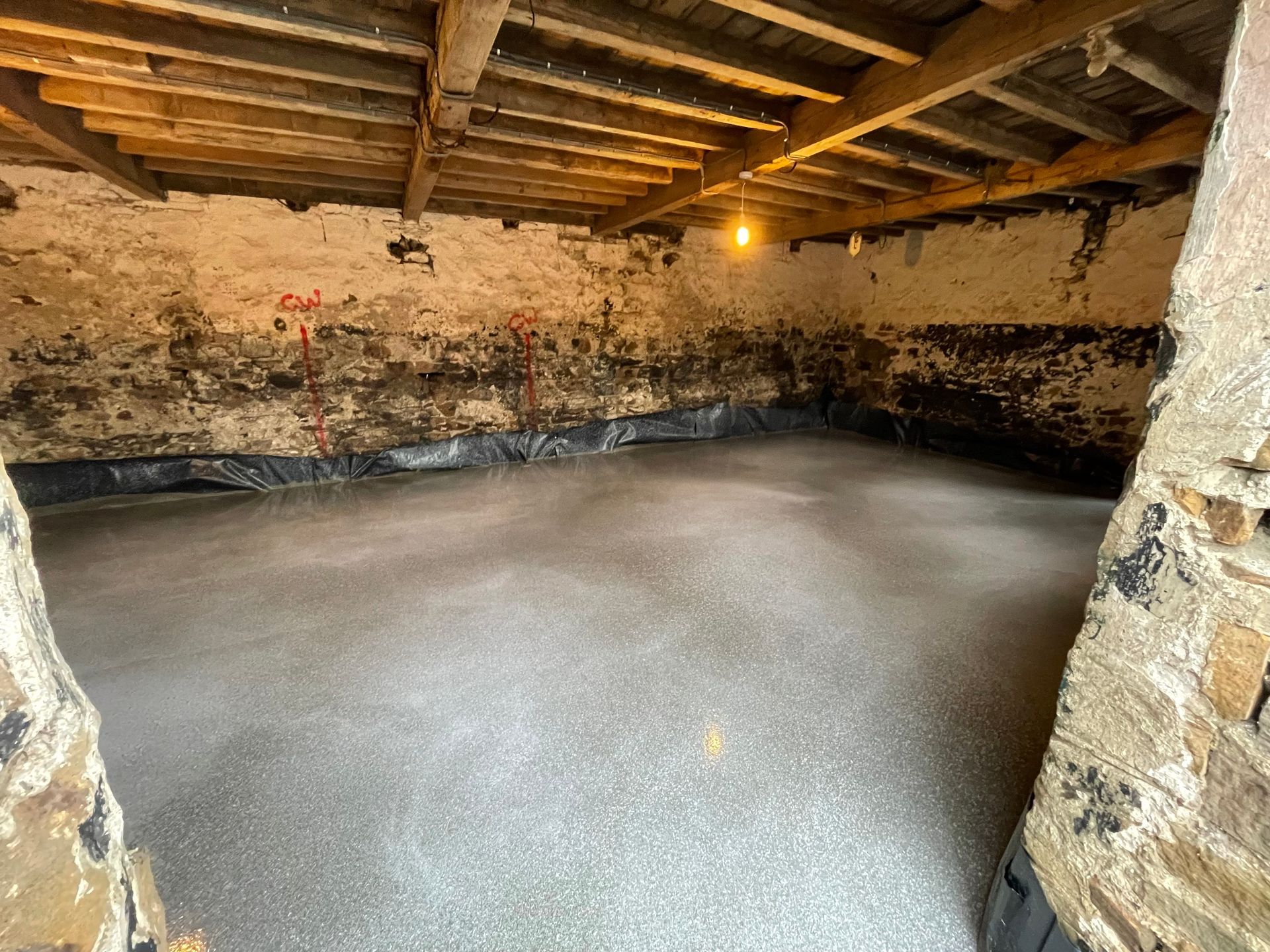 A newly poured concrete floor inside a stone-walled room, beneath a wooden ceiling.