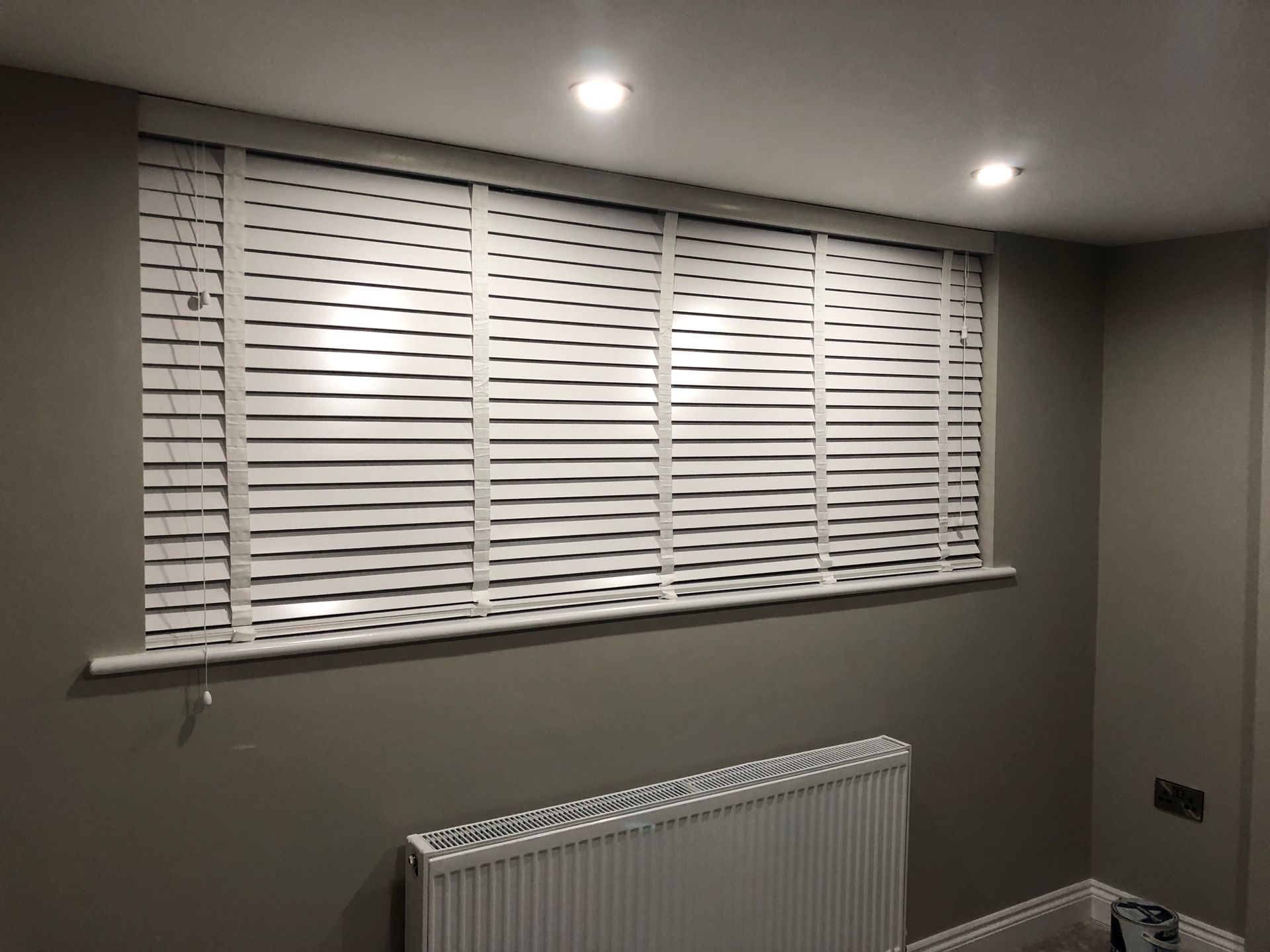 White window blinds in a room with a radiator and gray walls.