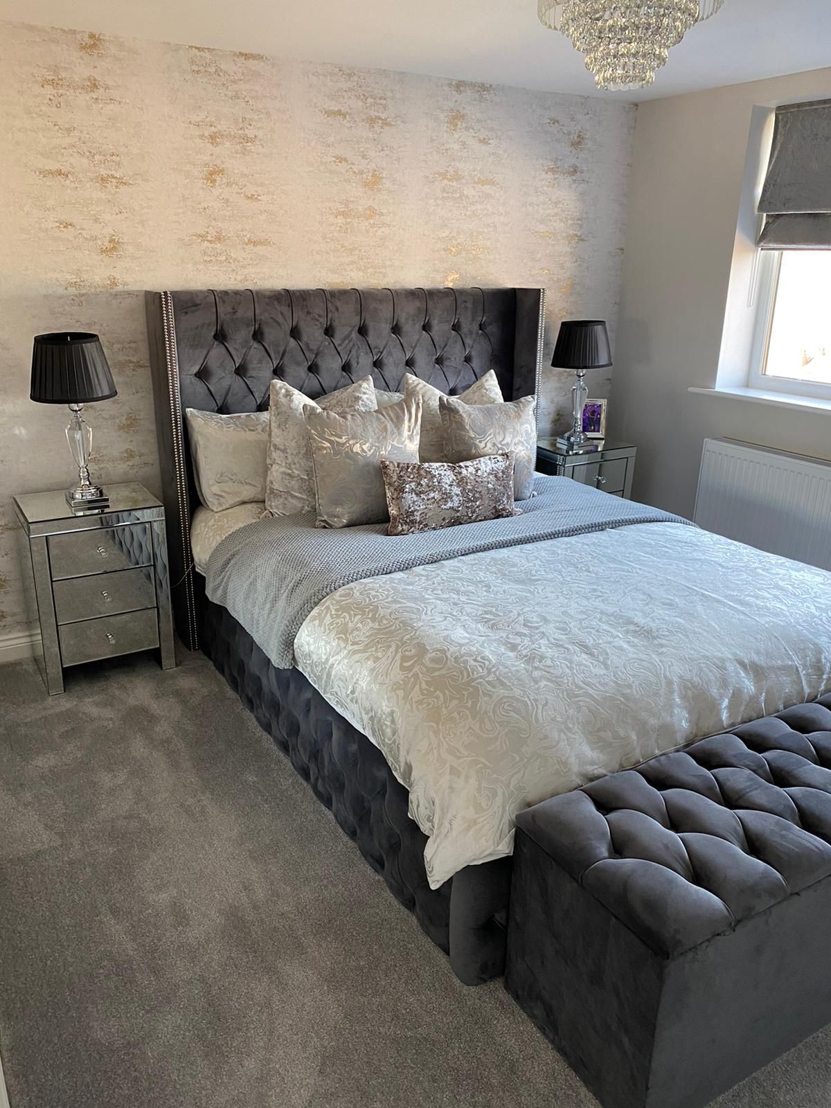 Gray bedroom with a velvet bed, tufted bench, mirrored nightstands, and textured wallpaper.