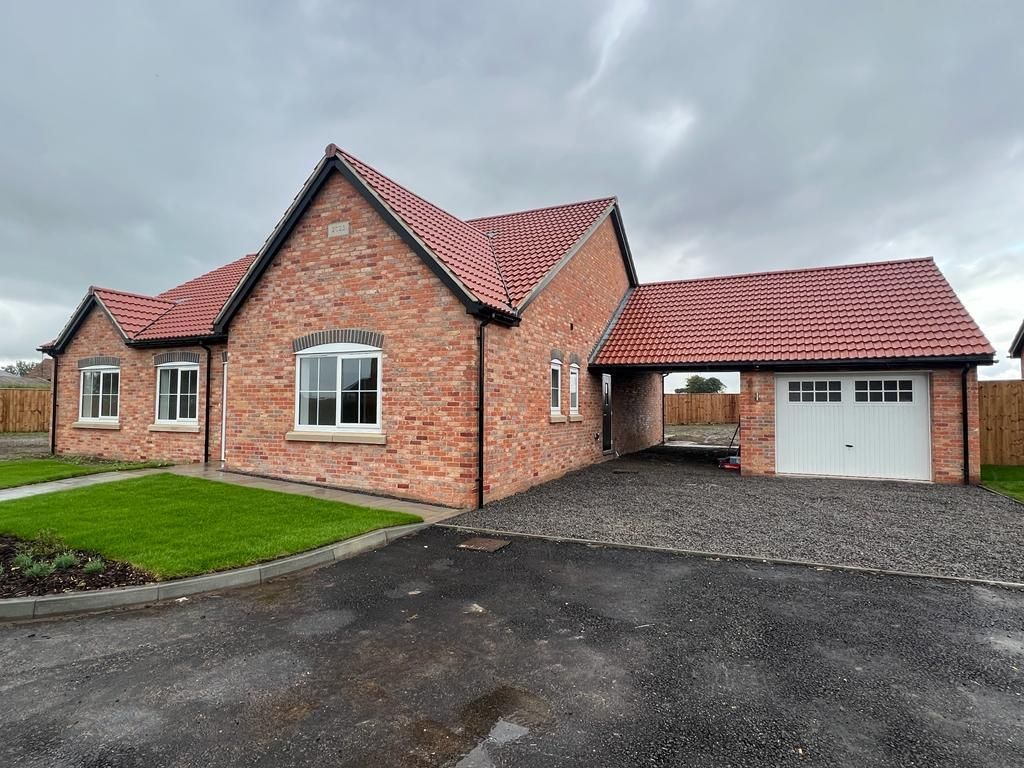 Red brick bungalow with a garage, red roof, and cloudy sky.