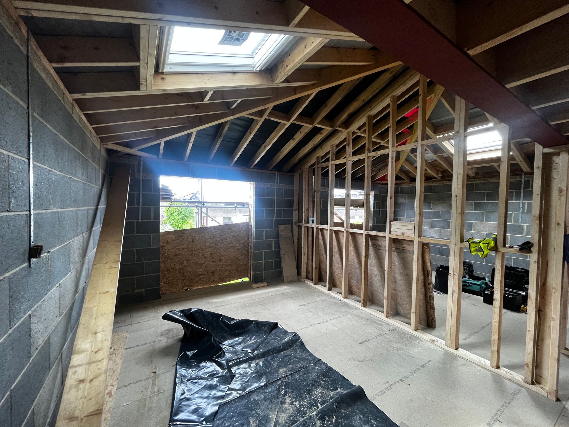 Construction site: interior room with exposed wooden beams, gray cinder block walls, and skylight.