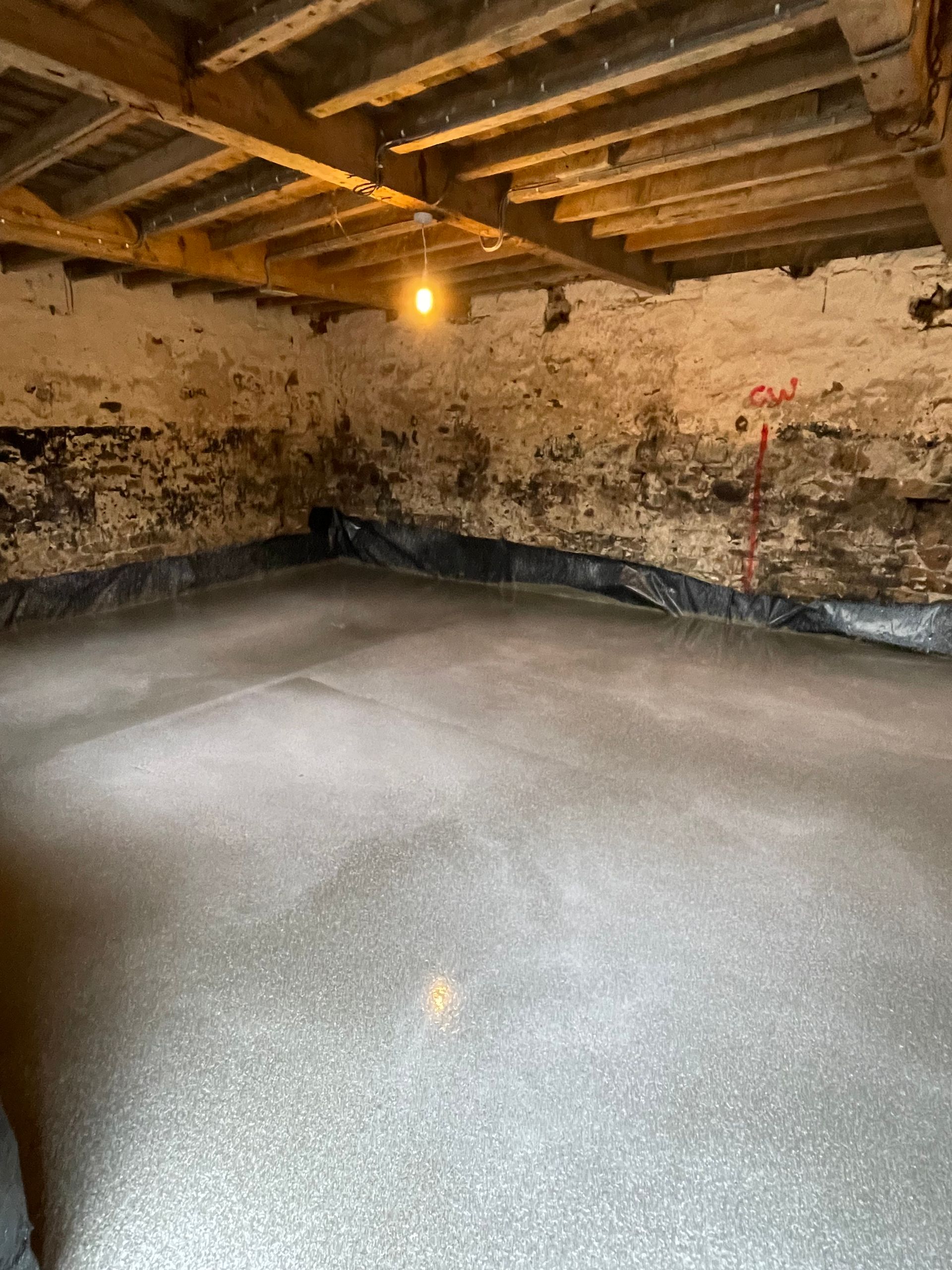 Freshly poured concrete floor in a basement, with a black barrier along the walls and old wooden beams overhead.