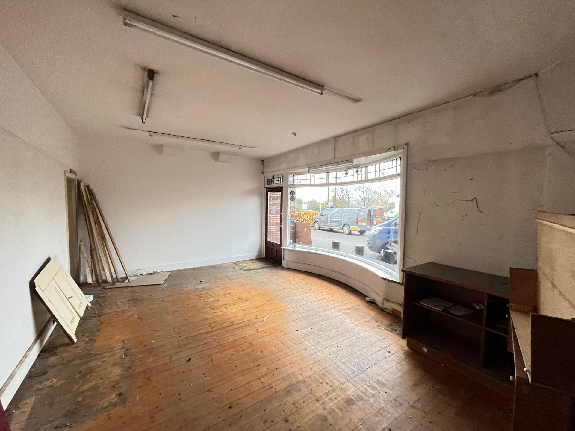 Empty interior of a shop with wooden floor, large curved window, and exposed pipes.