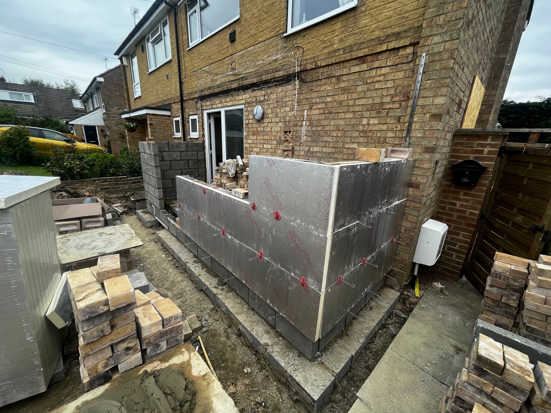 Brick construction project; external wall being built with insulation panels against a brick house.
