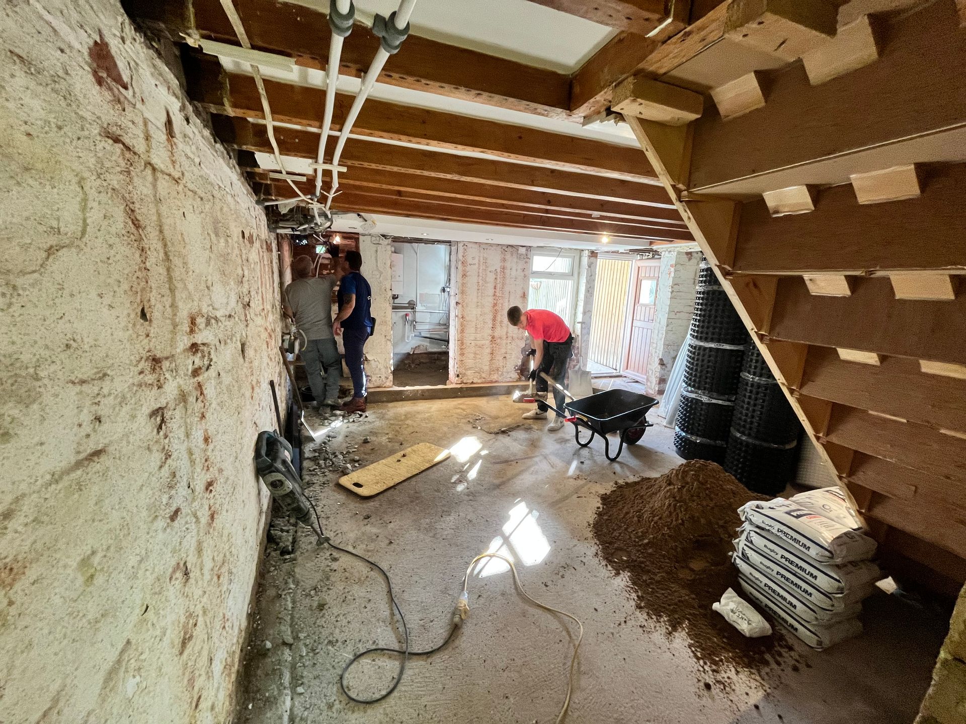 Construction workers renovating an interior space with exposed beams, concrete floor, and materials.