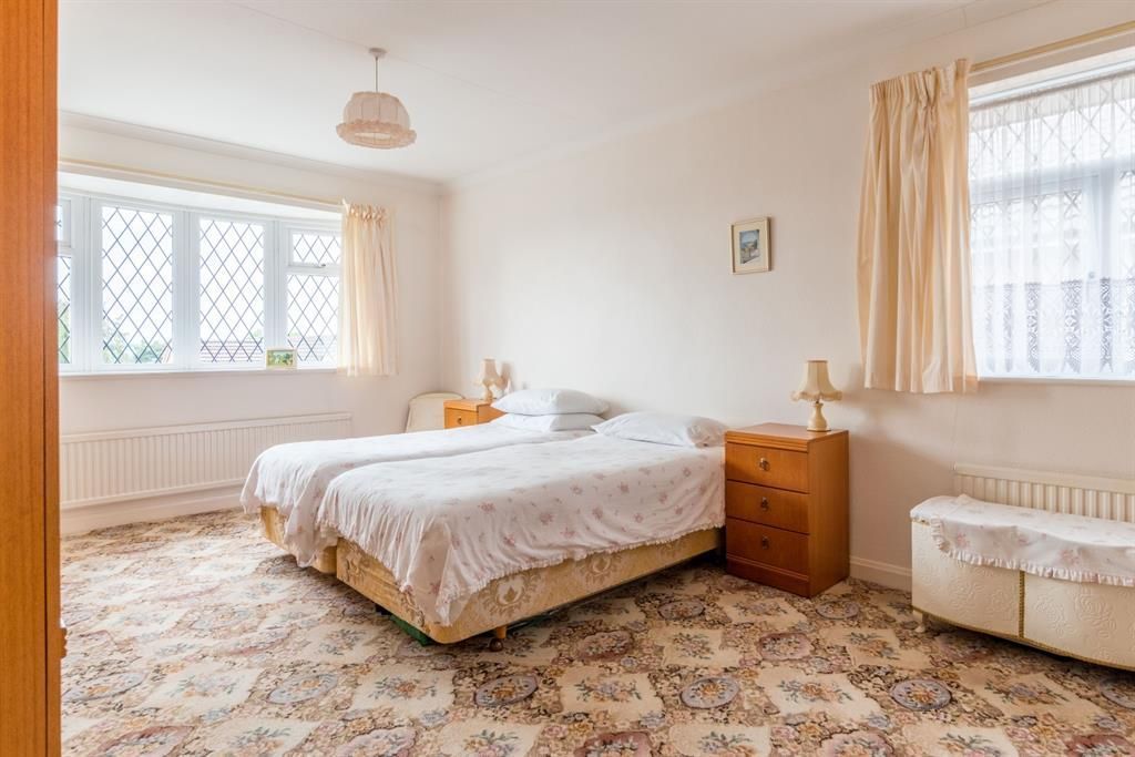 Bedroom with two twin beds, floral bedding, patterned carpet, windows with curtains, and two bedside tables.