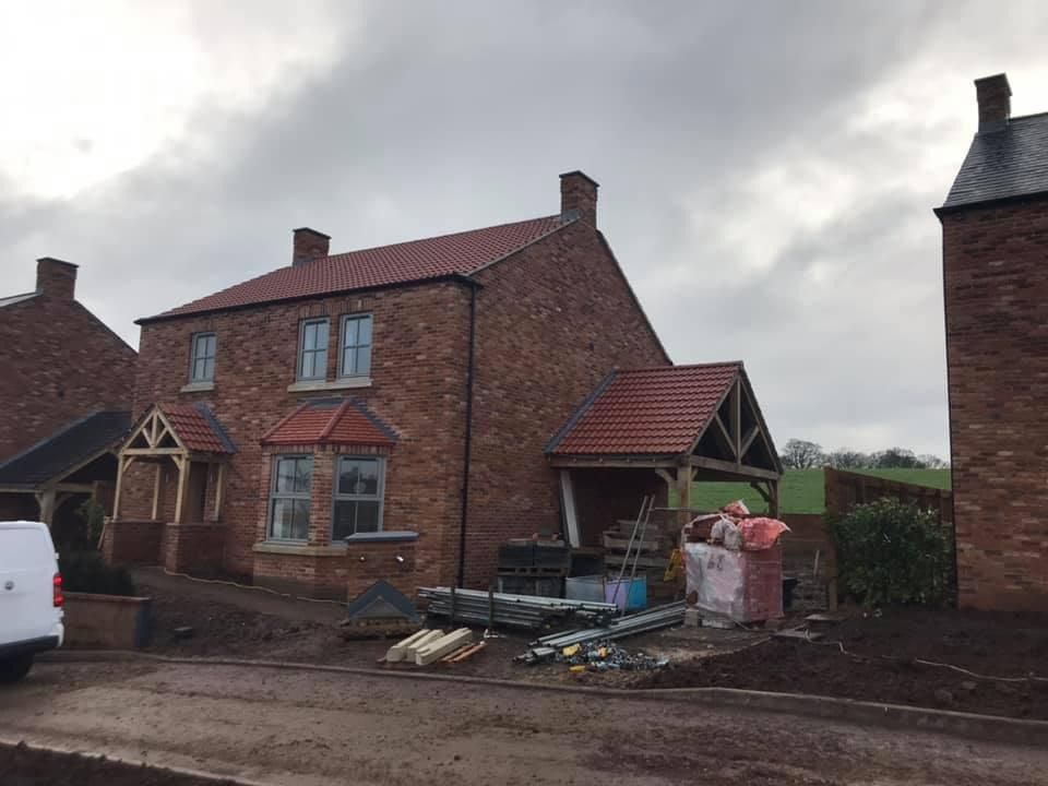 Brick house with red tile roof under construction, cloudy sky, construction materials in front.
