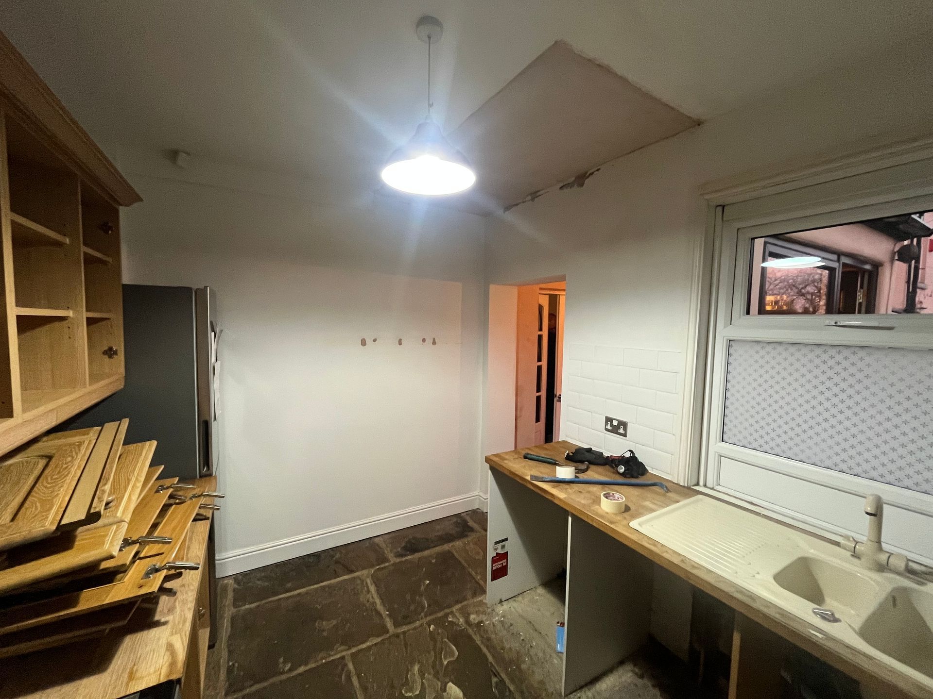 Kitchen during renovation with exposed ceiling, stone floor, and cabinets.