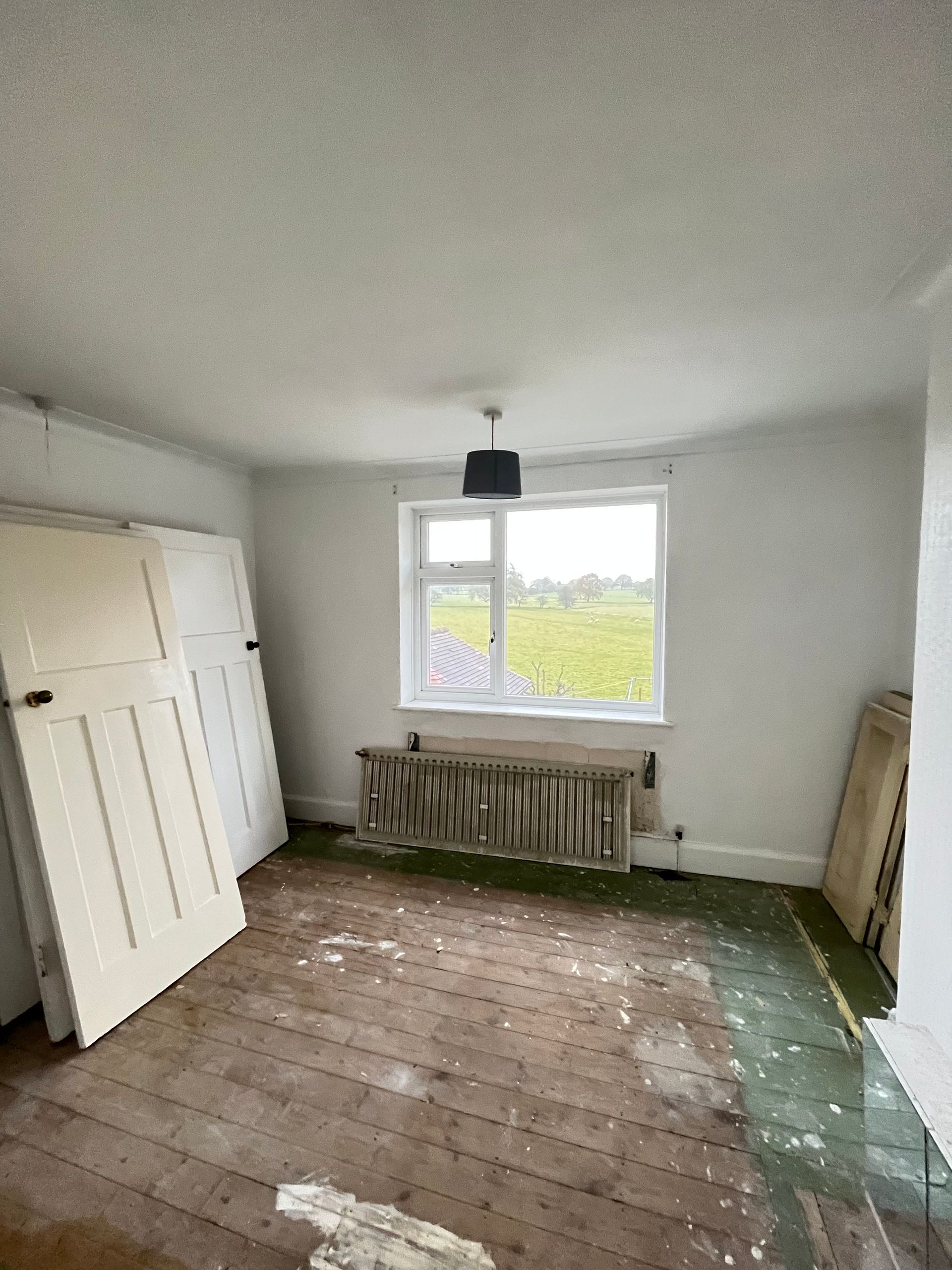 Empty room with weathered wooden floor, window, radiator, and three white doors leaning against the wall.