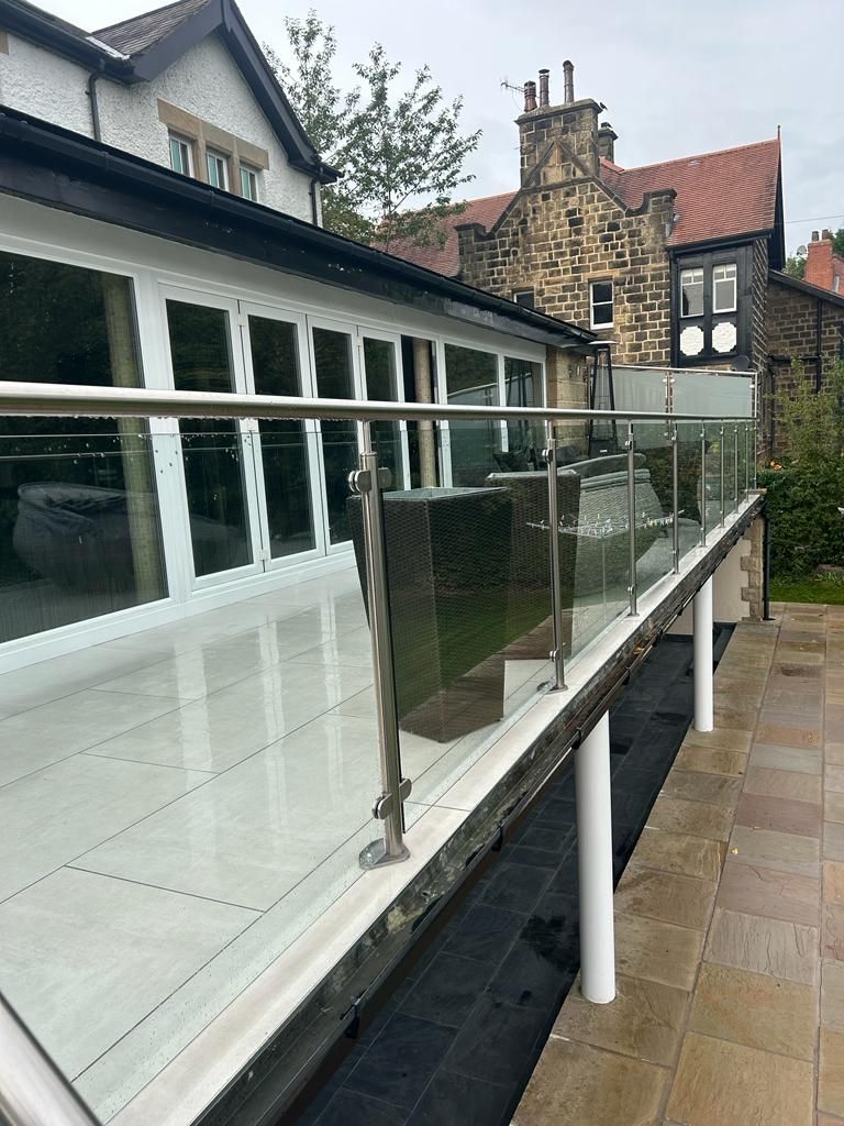 Glass railing with stainless steel posts on a white tiled patio, with stone building in the background.